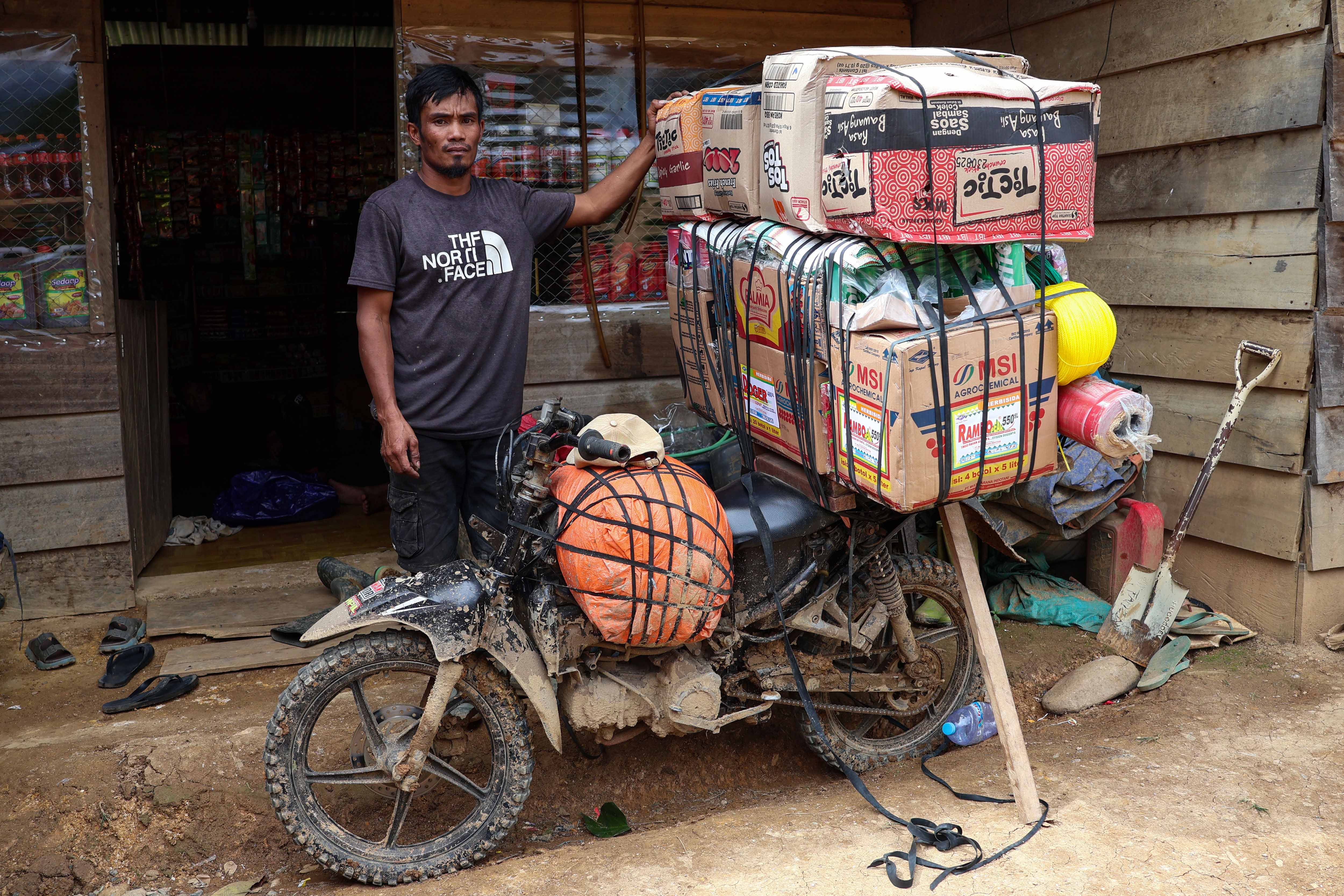 Muhammad Rapil (37) berdiri di dekat motornya yang mengangkut barang campuran saat tiba di rumahnya di Kecamatan Seko, Kabupaten Luwu Utara, Sulawesi Selatan.