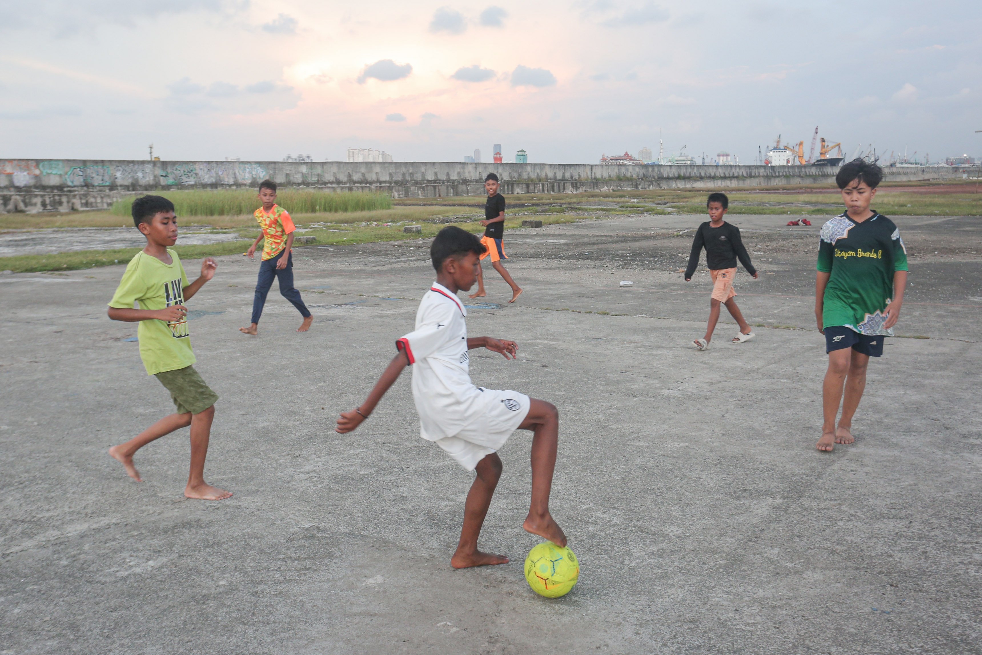 Anak-anak bermain sepak bola dengan latar belakang tanggul laut di kawasan Muara Baru, Penjaringan, Jakarta Utara, Senin (17/6/2025). Pemerintah Provinsi DKI Jakarta akan menggunakan surplus Anggaran Pendapatan dan Belanja Daerah (APBD) dan pendapatan dari pengolahan sampah menjadi energi listrik untuk membiayai pembangunan Giant Sea Wall atau tanggul laut raksasa.