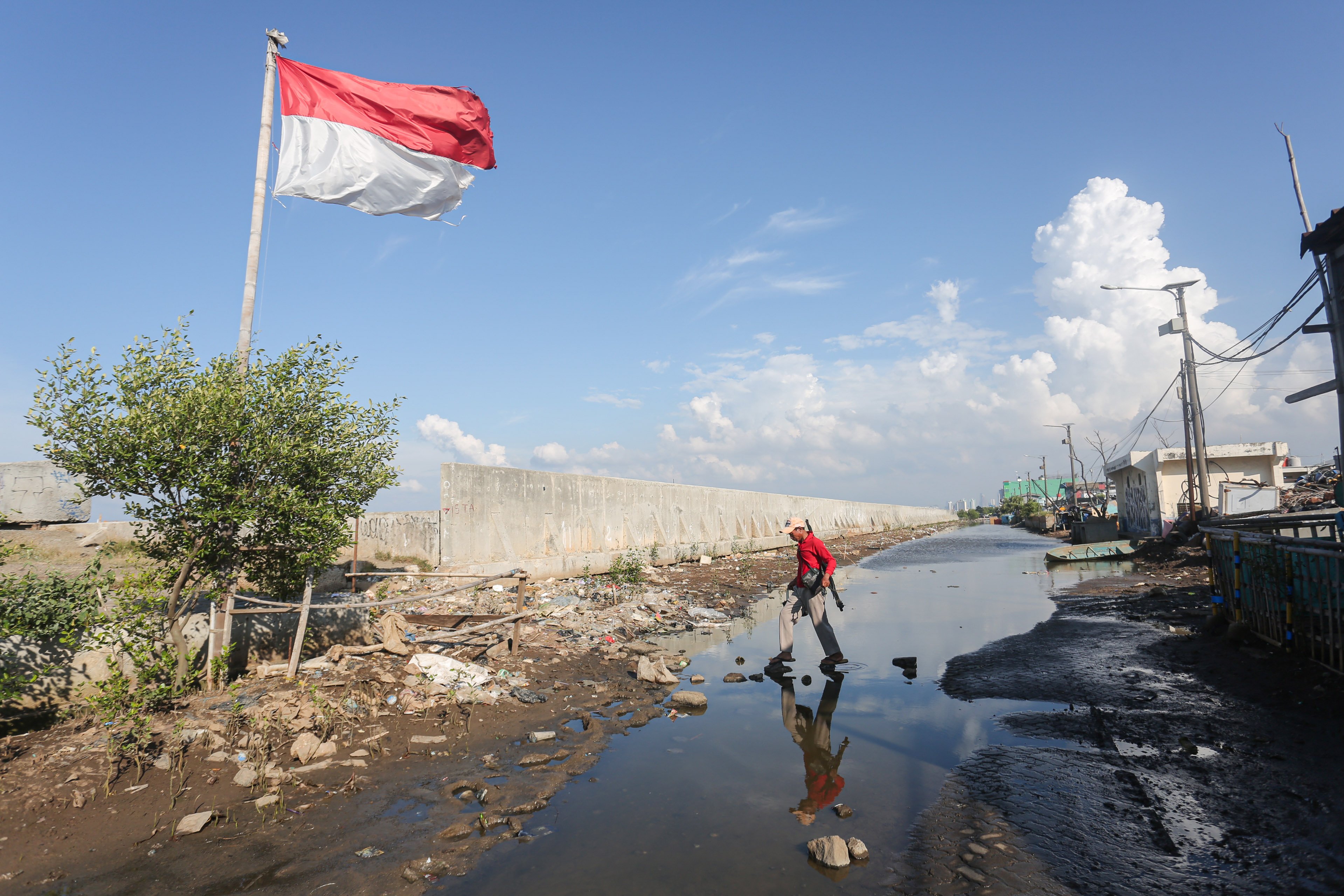 Warga berjalan di dekat tanggul laut di kawasan Muara Baru, Penjaringan, Jakarta Utara, Senin (17/6/2025). Pemerintah Provinsi DKI Jakarta akan menggunakan surplus Anggaran Pendapatan dan Belanja Daerah (APBD) dan pendapatan dari pengolahan sampah menjadi energi listrik untuk membiayai pembangunan Giant Sea Wall atau tanggul laut raksasa.