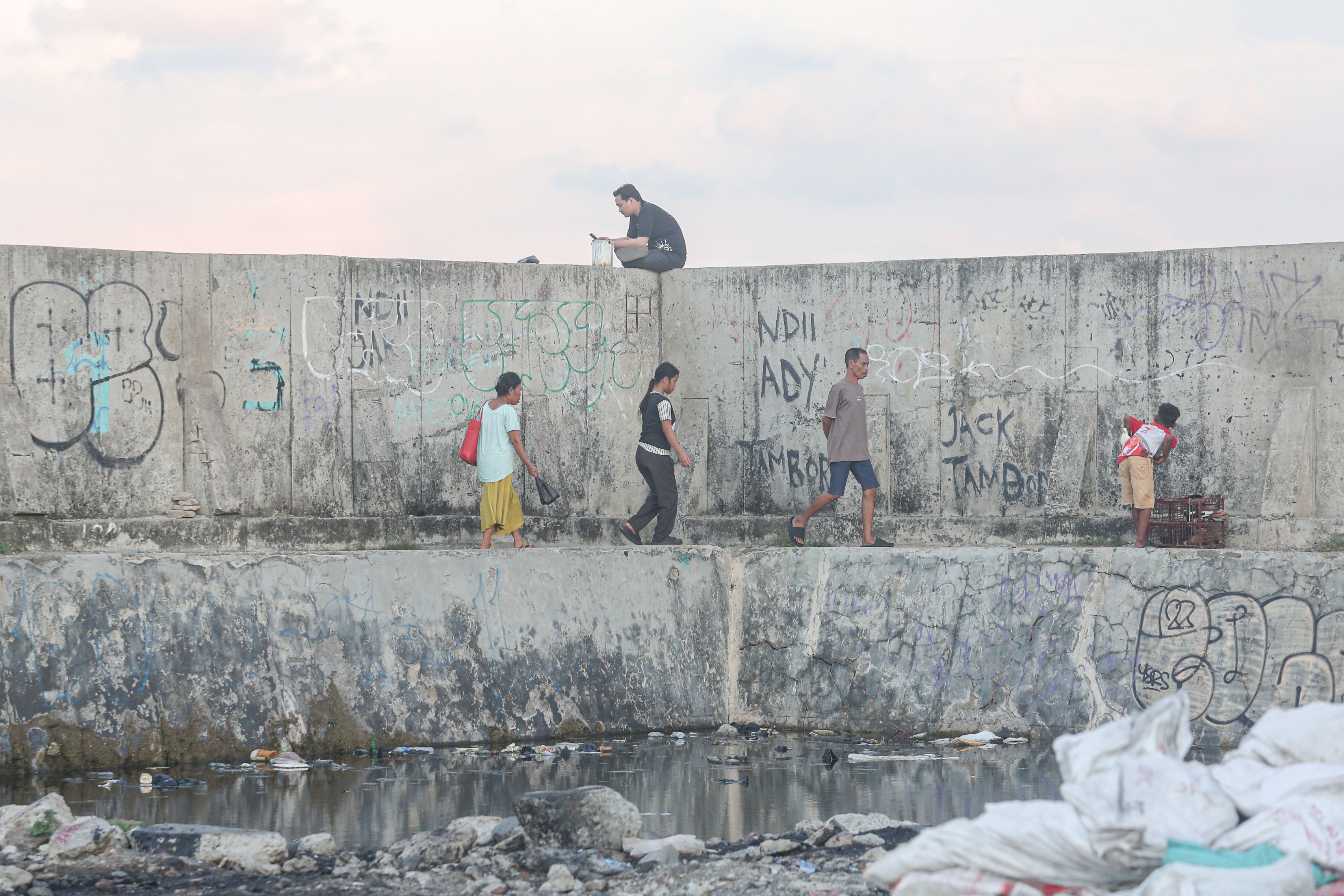 Warga berjalan di dekat tanggul laut di kawasan Muara Baru, Penjaringan, Jakarta Utara, Senin (17/6/2025). Pemerintah Provinsi DKI Jakarta akan menggunakan surplus Anggaran Pendapatan dan Belanja Daerah (APBD) dan pendapatan dari pengolahan sampah menjadi energi listrik untuk membiayai pembangunan Giant Sea Wall atau tanggul laut raksasa.