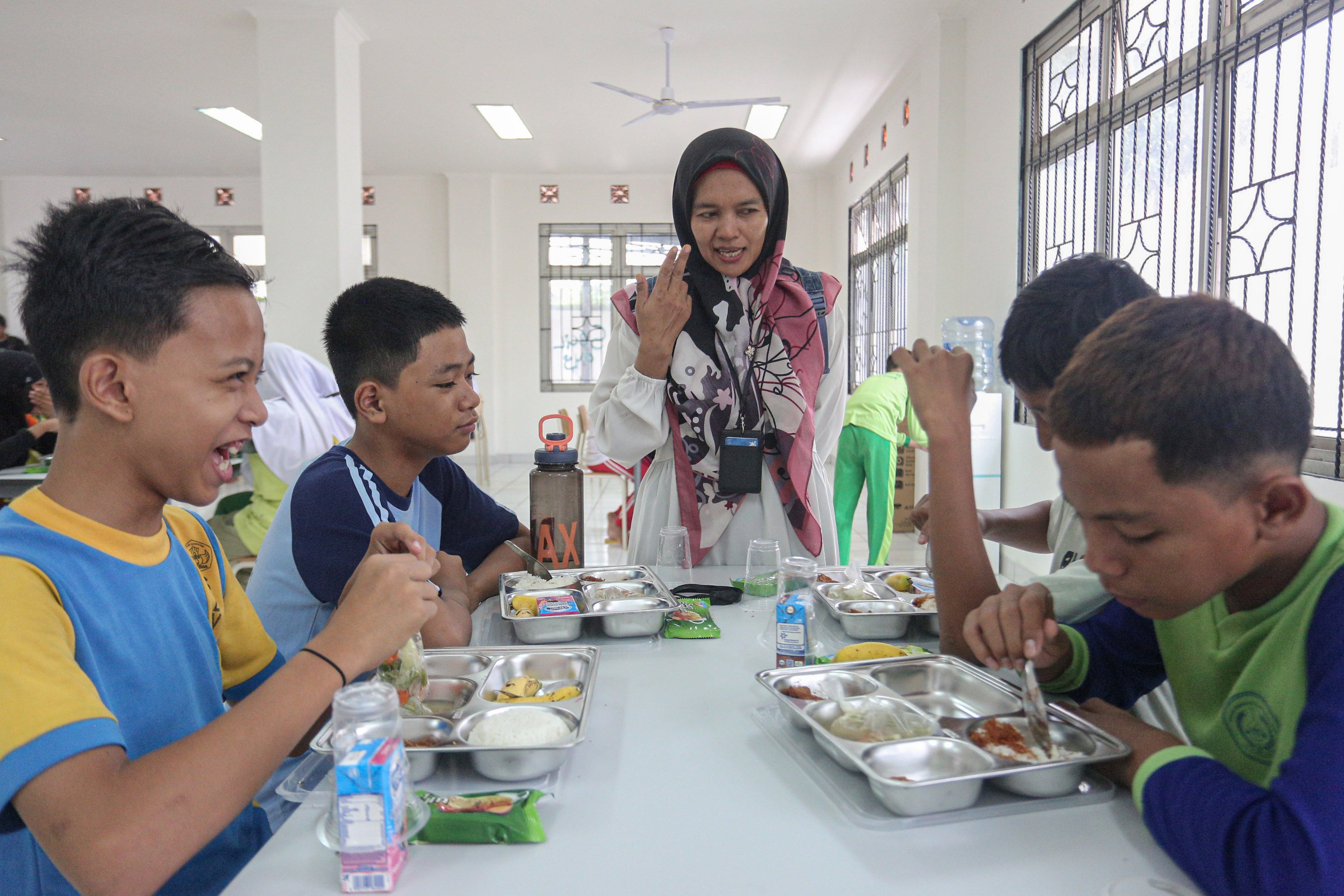 Seorang guru (tengah) meninjau kegiatan makan siang siswa pada Masa Pengenalan Lingkungan Sekolah (MPLS) di Sekolah Rakyat Menengah Pertama 6, Sentra Handayani, Bambu Apus, Jakarta Timur, Senin (14/7/2025). Pemerintah resmi memulai program Sekolah Rakyat pada tahap pertama yang dirancang sebagai sekolah berasrama dan diperuntukkan bagi siswa dari keluarga berpenghasilan rendah di 100 titik lokasi yang tersebar di seluruh wilayah Indonesia.