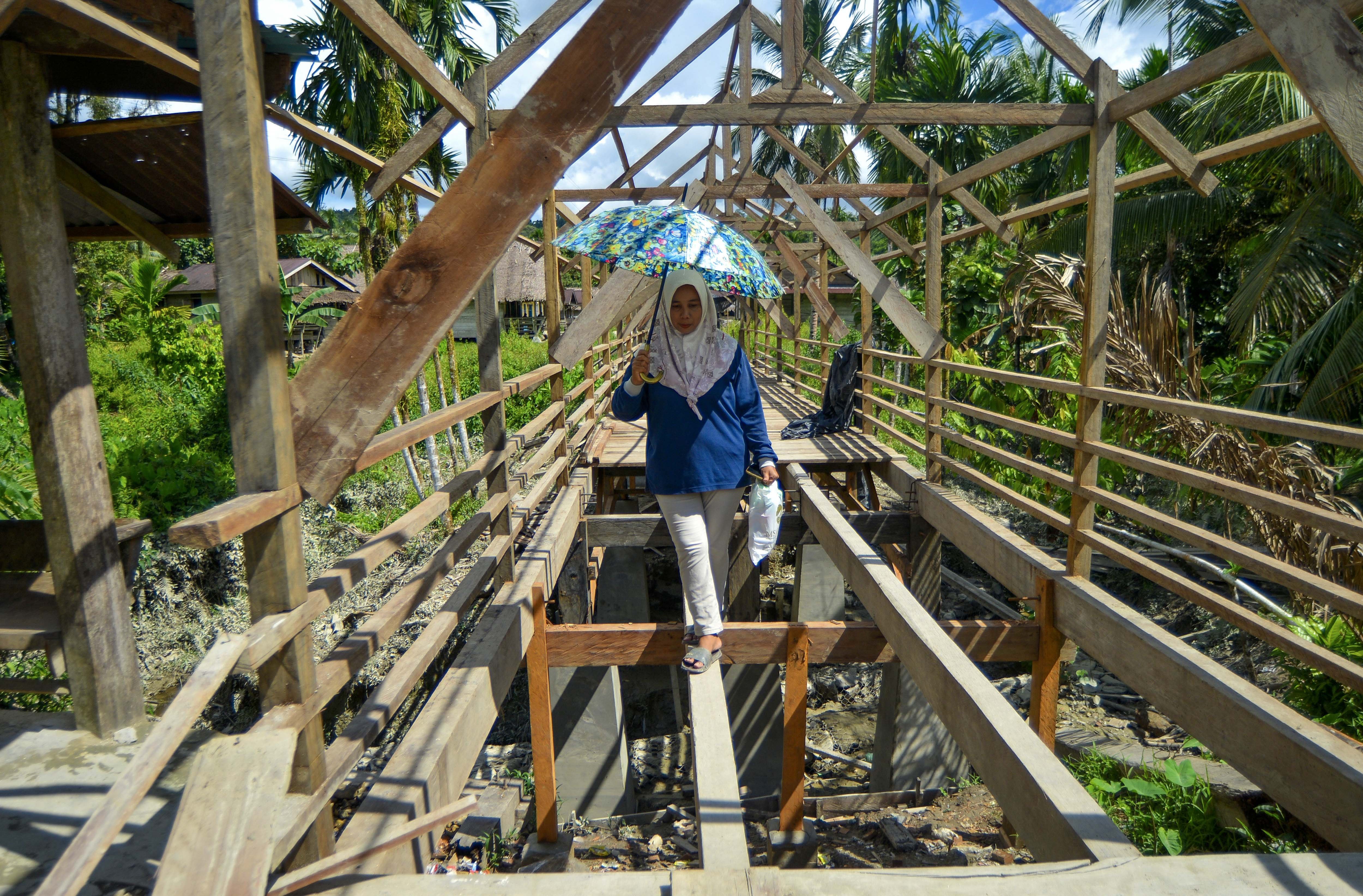 Bidan Ilen, berjalan melewati jembatan yang belum jadi saat akan mengobati warga di Desa Matotonan, Siberut Selatan, Mentawai, Sumatera Barat.