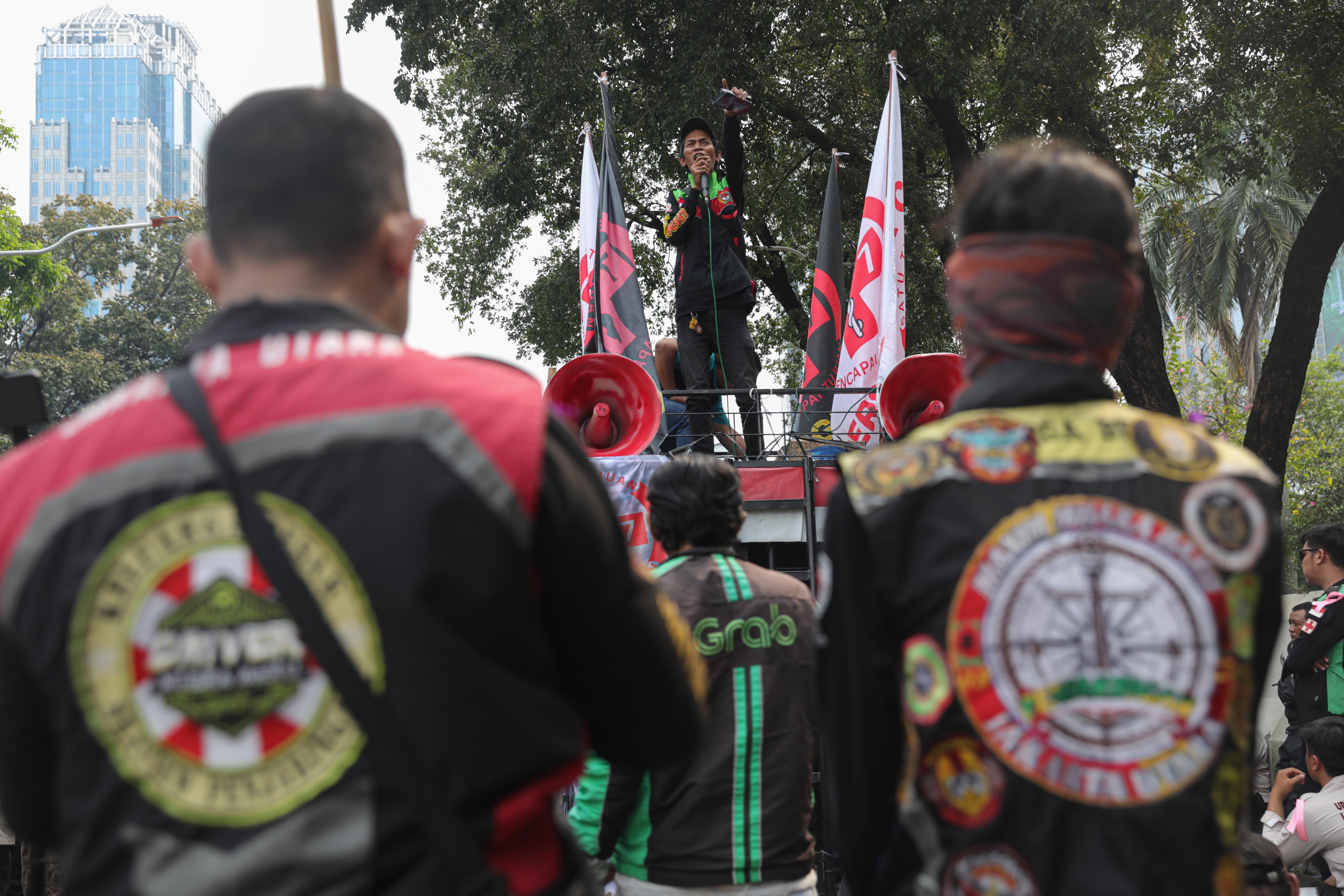 Seorang pengemudi ojek online (ojol) yang tergabung dalam Unit Reaksi Cepat (URC) Bergerak menyampaikan orasi saat demonstrasi di kawasan Patung Kuda, Jakarta Pusat, Kamis (17/7/2025). Dalam aksinya tersebut mereka menyampaikan sejumlah tuntutan yakni menolak perubahan status ojol menjadi buruh atau pekerja dan wacana potongan aplikator dari 10% menjadi 20% serta mendesak Presiden Prabowo Subianto mengeluarkan Perppu yang mengatur tentang ojol.