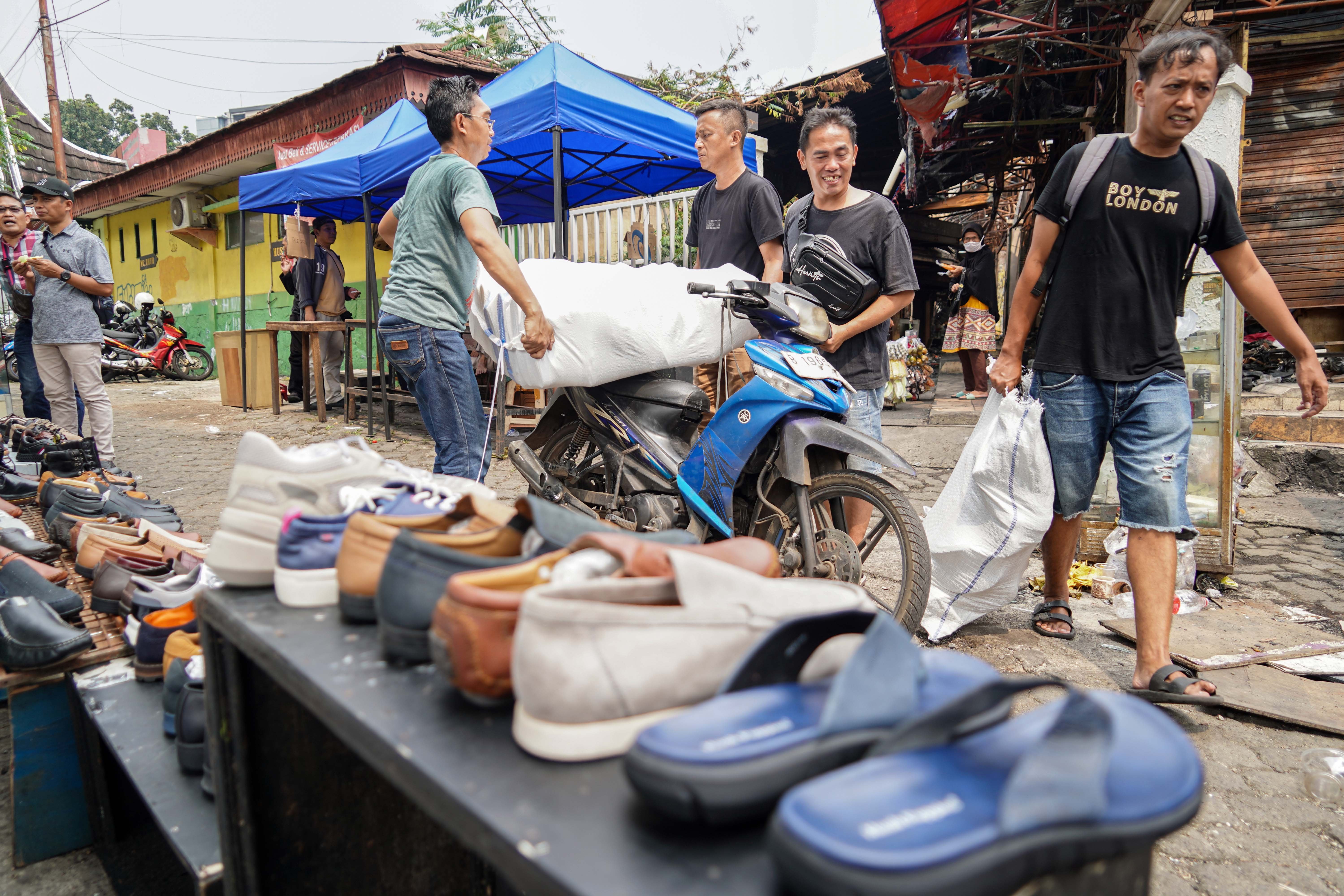 Pedagang mengangkut sepatu yang akan dijual di Pasar Taman Puring, Kebayoran Baru, Jakarta Selatan, Senin (4/8/2025). Sepekan pascakebakaran yang menghanguskan 552 kios pada Senin (28/7/2025) malam, sejumlah pedagang memanfaatkan trotoar di depan pasar untuk menjajakan barang dagangannya sambil menanti kejelasan pasar tersebut dibangun kembali.