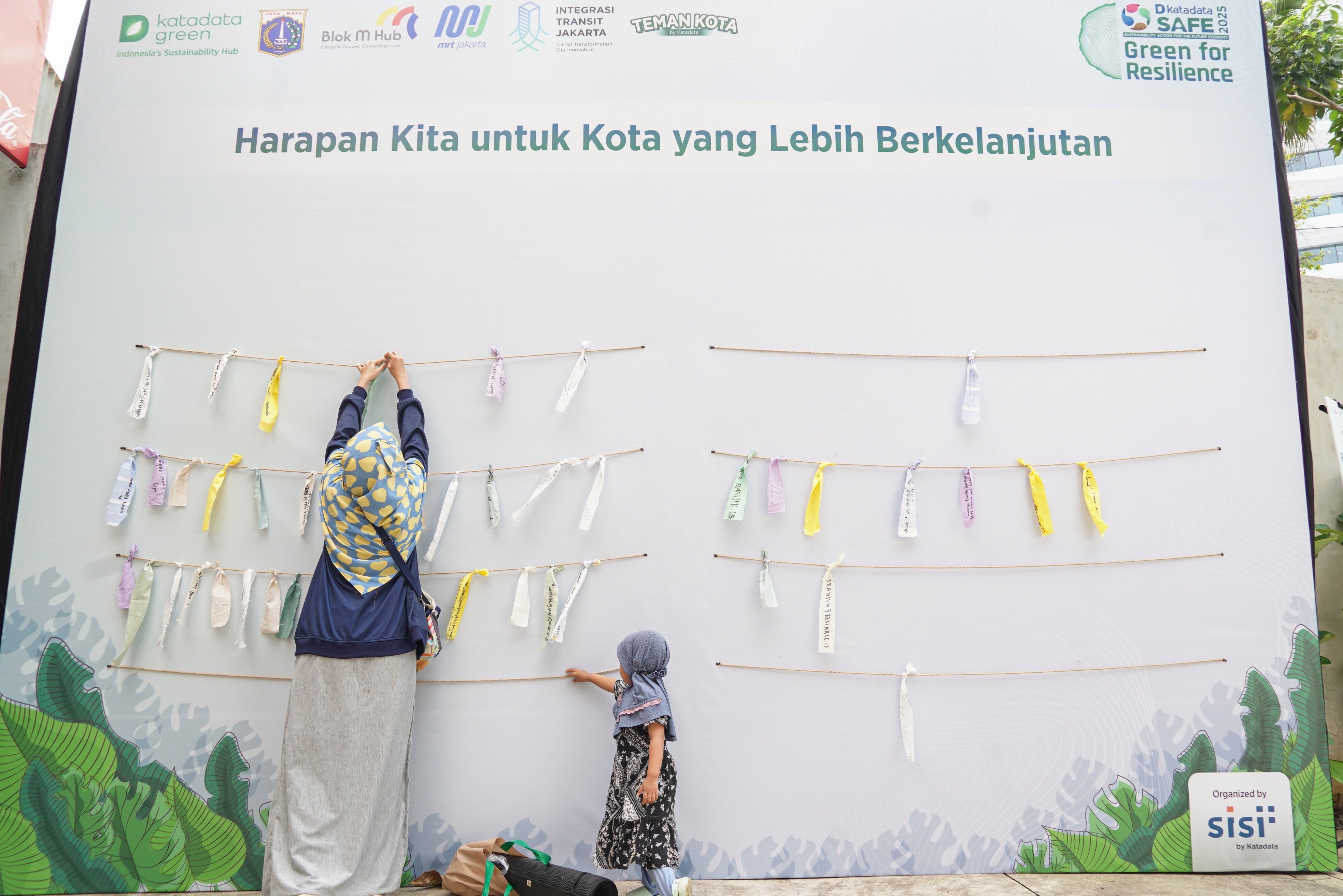 Pengunjung mengikatkan sehelai kain yang berisi pesan untuk kota yang berkelanjutan pada acara Katadata Green Collabs Blok M: Selaras Urban 2025 di Taman Literasi Martha Christina Tiahahu, Blok M, Jakarta, Sabtu (23/8/2025). Acara yang digelar sebagai wadah kolaborasi untuk menciptakan keselarasan antara alam, kota, serta kehidupan manusia ini diisi oleh berbagai aktivitas mulai dari sesi diskusi, zona ekspresi, zona healing, zona alam hingga zona musik.