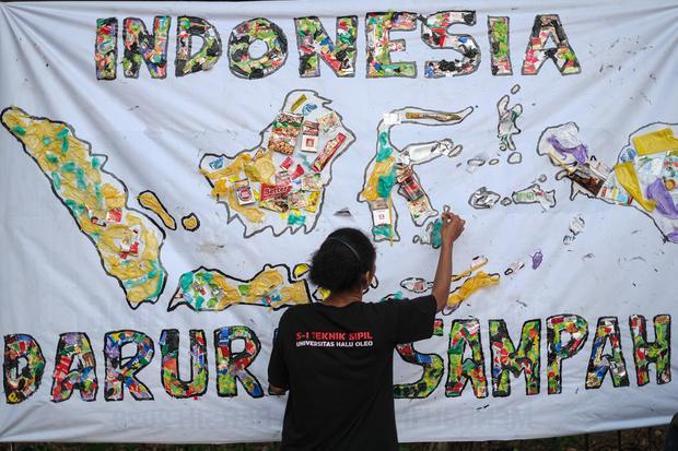 Seorang mahasiswa menempelkan sampah plastik pada baliho saat kampanye darurat sampah di pelataran Eks MTQ Kendari, Sulawesi Tenggara, Minggu (21/9/2025). Dalam kampanyenya mahasiswa dan pemerhati lingkungan di wilayah itu, menyuarakan pesan mengenai kond
