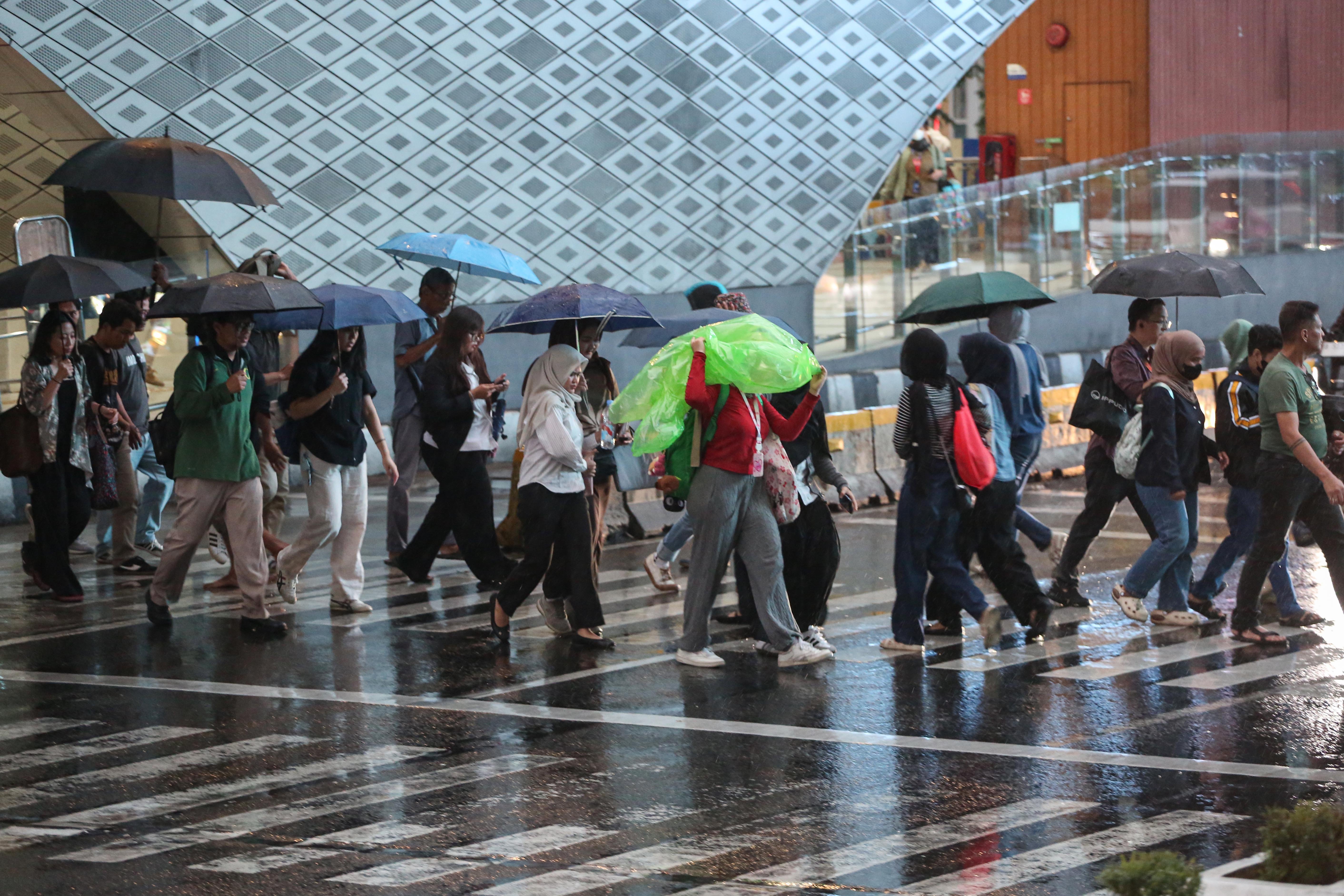 Warga memakai payung saat hujan di kawasan Bundaran HI, Jakarta, Rabu (29/10/2025). Menteri Kesehatan, Budi Gunadi Sadikin menghimbau kepada masyarakat untuk mengenakan masker dan mengurangi aktivitas setelah hujan menyusul temuan Badan Riset dan Inovasi Nasional (BRIN) yang mengungkap air hujan di Jakarta mengandung mikroplastik.