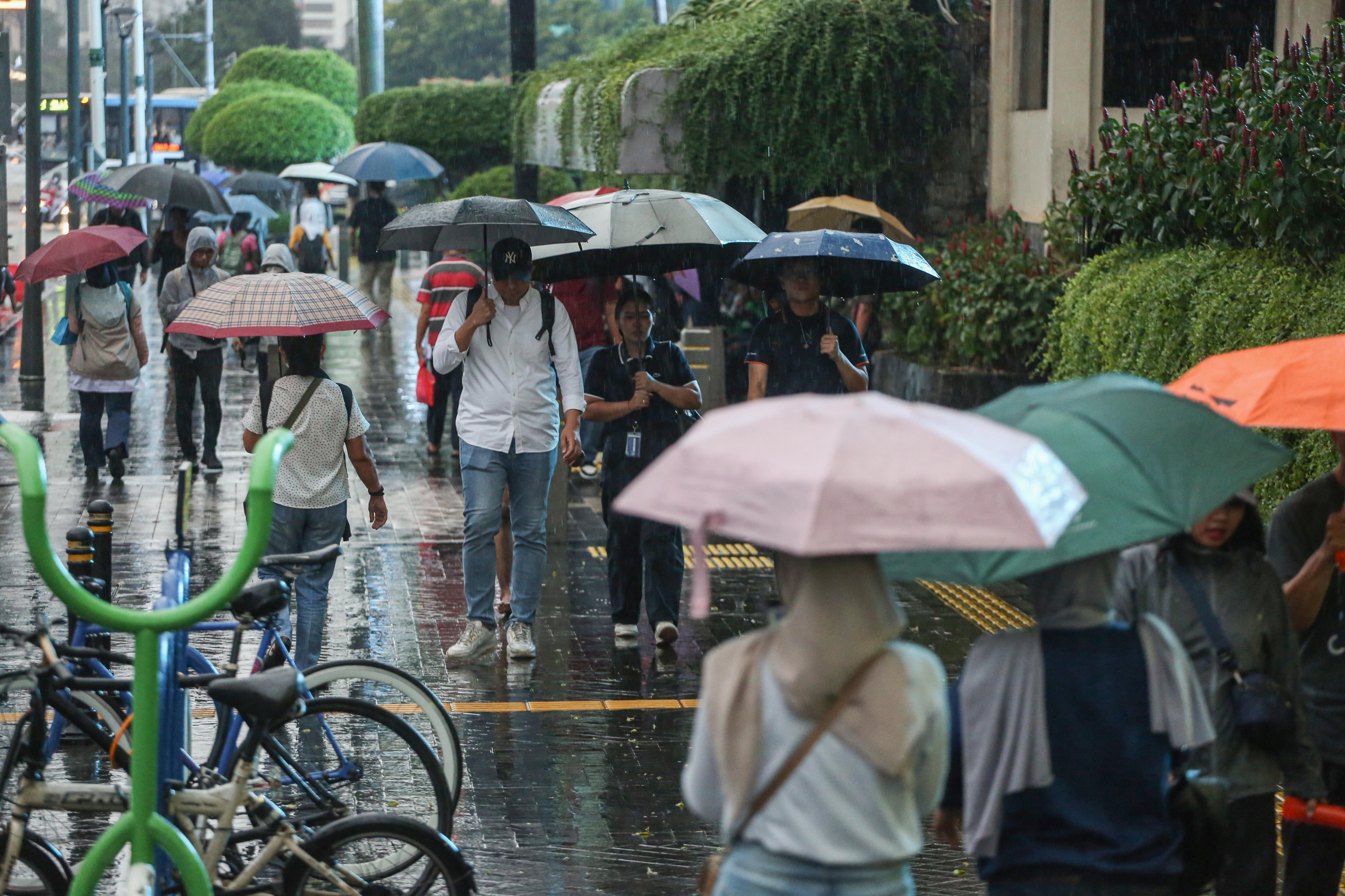 Warga memakai payung saat hujan di kawasan Bundaran HI, Jakarta, Rabu (29/10/2025). Menteri Kesehatan, Budi Gunadi Sadikin menghimbau kepada masyarakat untuk mengenakan masker dan mengurangi aktivitas setelah hujan menyusul temuan Badan Riset dan Inovasi Nasional (BRIN) yang mengungkap air hujan di Jakarta mengandung mikroplastik.