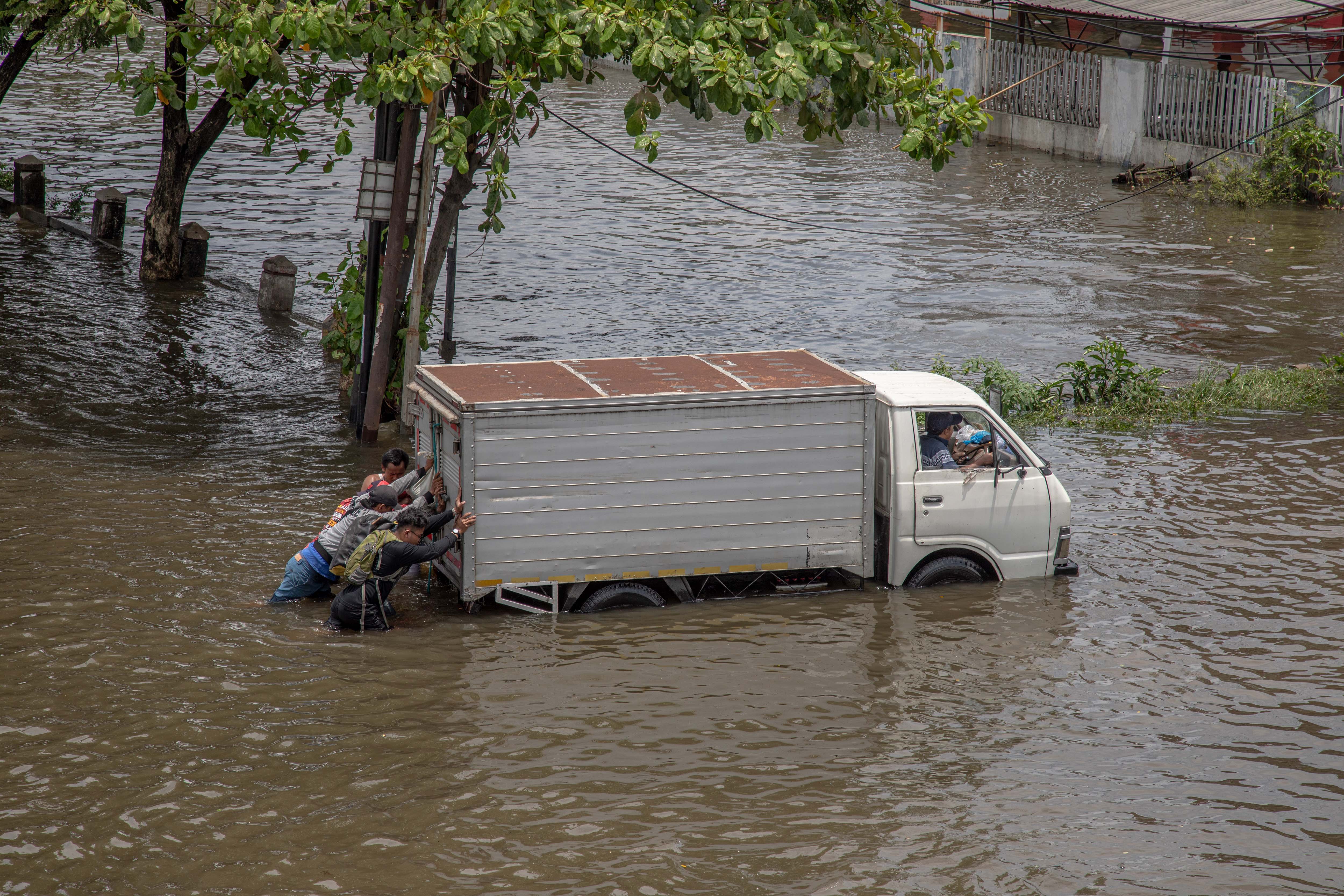 Warga bergotong royong mendorong truk yang mogok seusai menembus genangan banjir jalur utama pantura Semarang-Surabaya, Jalan Kaligawe Raya, Semarang, Jawa Tengah, Kamis (23/10/2025). Puluhan kendaraan bermotor roda dua, roda empat, hingga truk mengalami mogok mesin karena memaksakan menembus genangan banjir di jalur tersebut. 