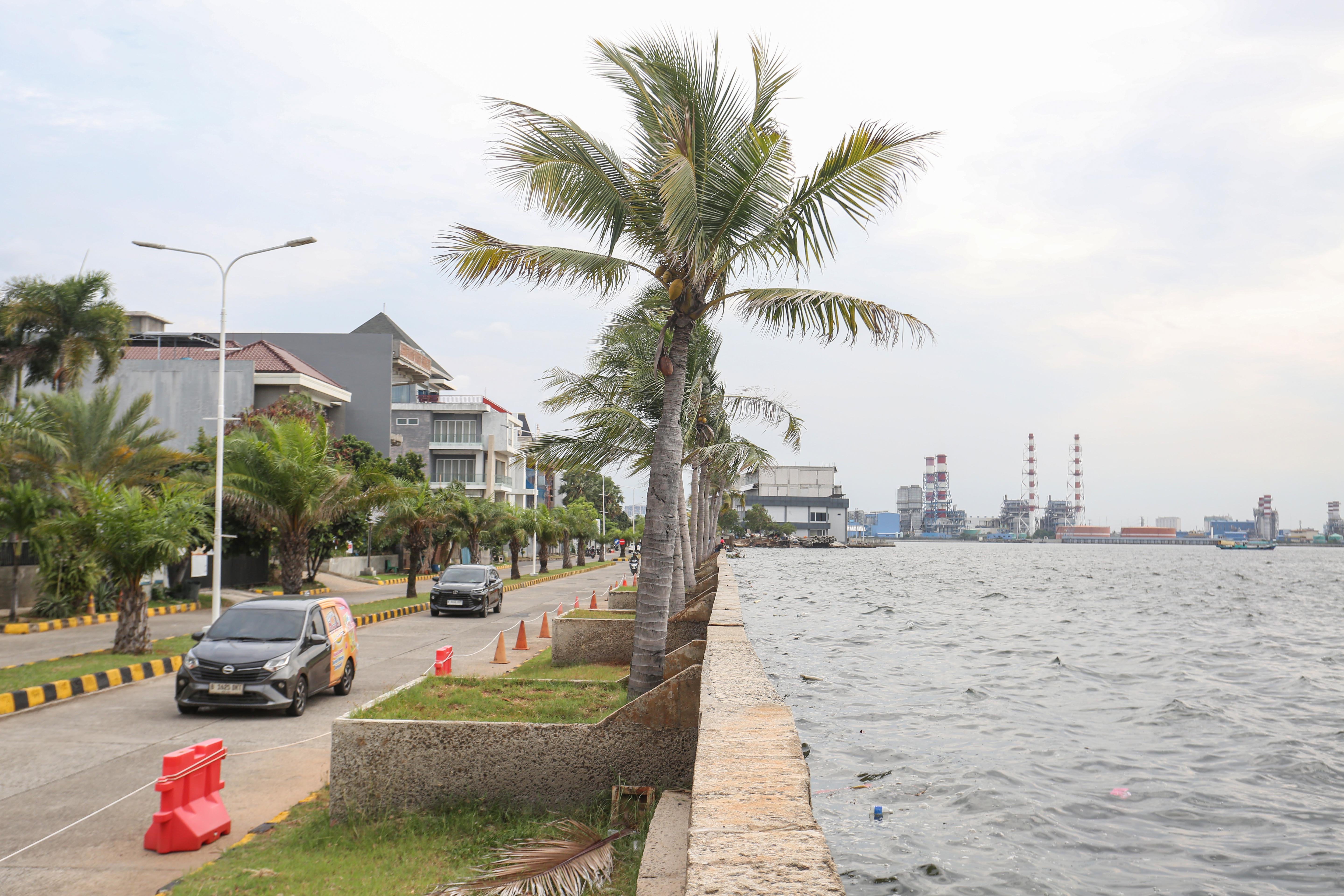 Mobil melintas di dekat tanggul di kawasan Pantai Mutiara, Penjaringan, Jakarta Utara, Rabu (26/11/2025). Fenomena pasang maksimum air laut bersamaan dengan fase bulan baru dan turunnya permukaan tanah di Jakarta setiap tahunnya membuat air laut berada di posisi yang lebih tinggi dari jalan di kawasan tersebut.