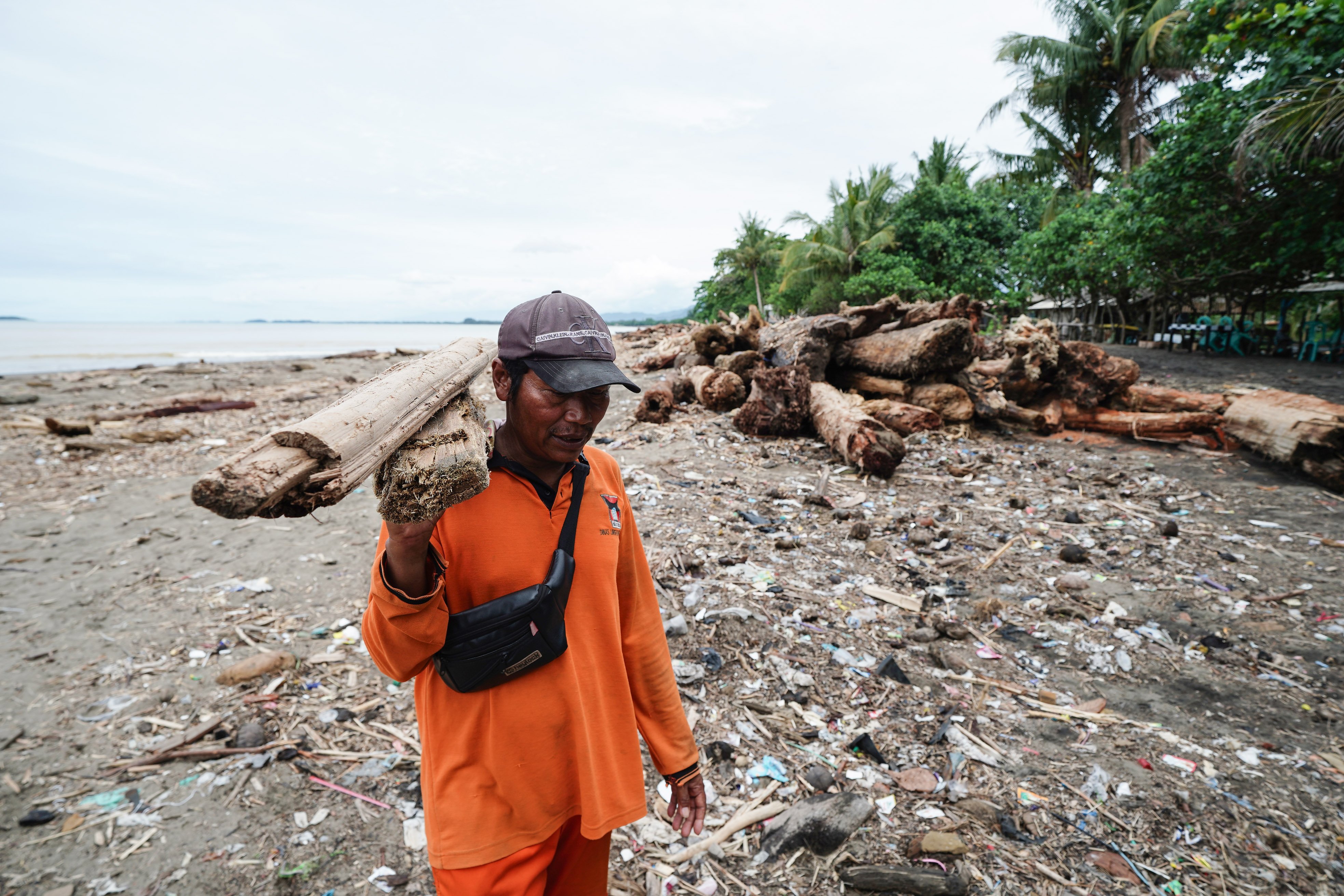Petugas Dinas Lingkungan Hidup membersihkan kayu sisa banjir bandang di bibir Pantai Parkit, Padang Sumatera Barat, Senin (8/12/2025). Selain mengumpulkan material kayu tersebut, petugas DLH juga mengambil sampel kayu untuk diperiksa oleh pihak berwenang. 