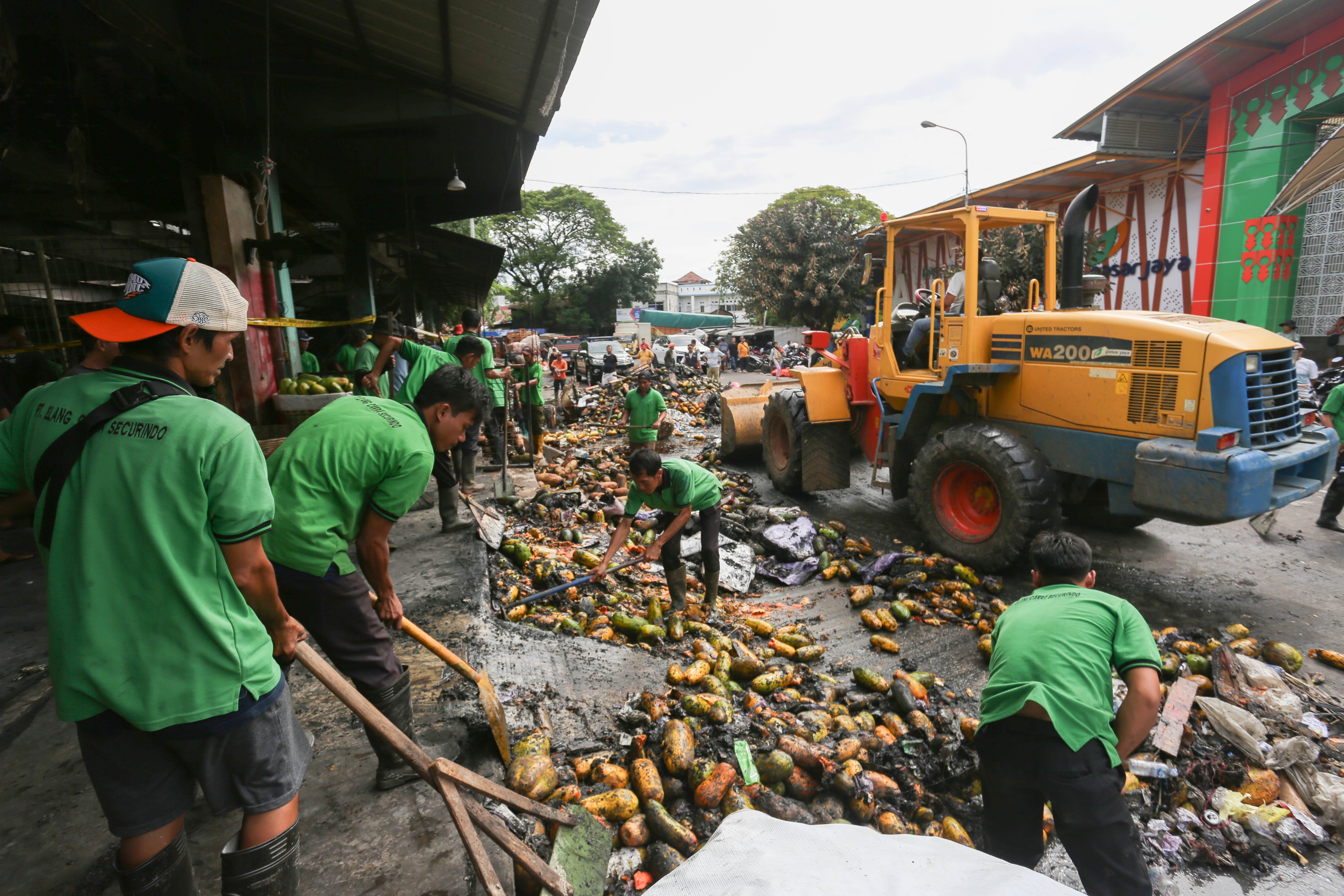 Petugas membersihkan buah pepaya usai kios pedagang terbakar di Pasar Induk Kramat Jati, Jakarta Timur, Senin (15/12/2025). Kebakaran yang diduga akibat korsleting listrik tersebut menyebabkan 350 kios pedagang hangus terbakar dengan kerugian mencapai Rp10 miliar.