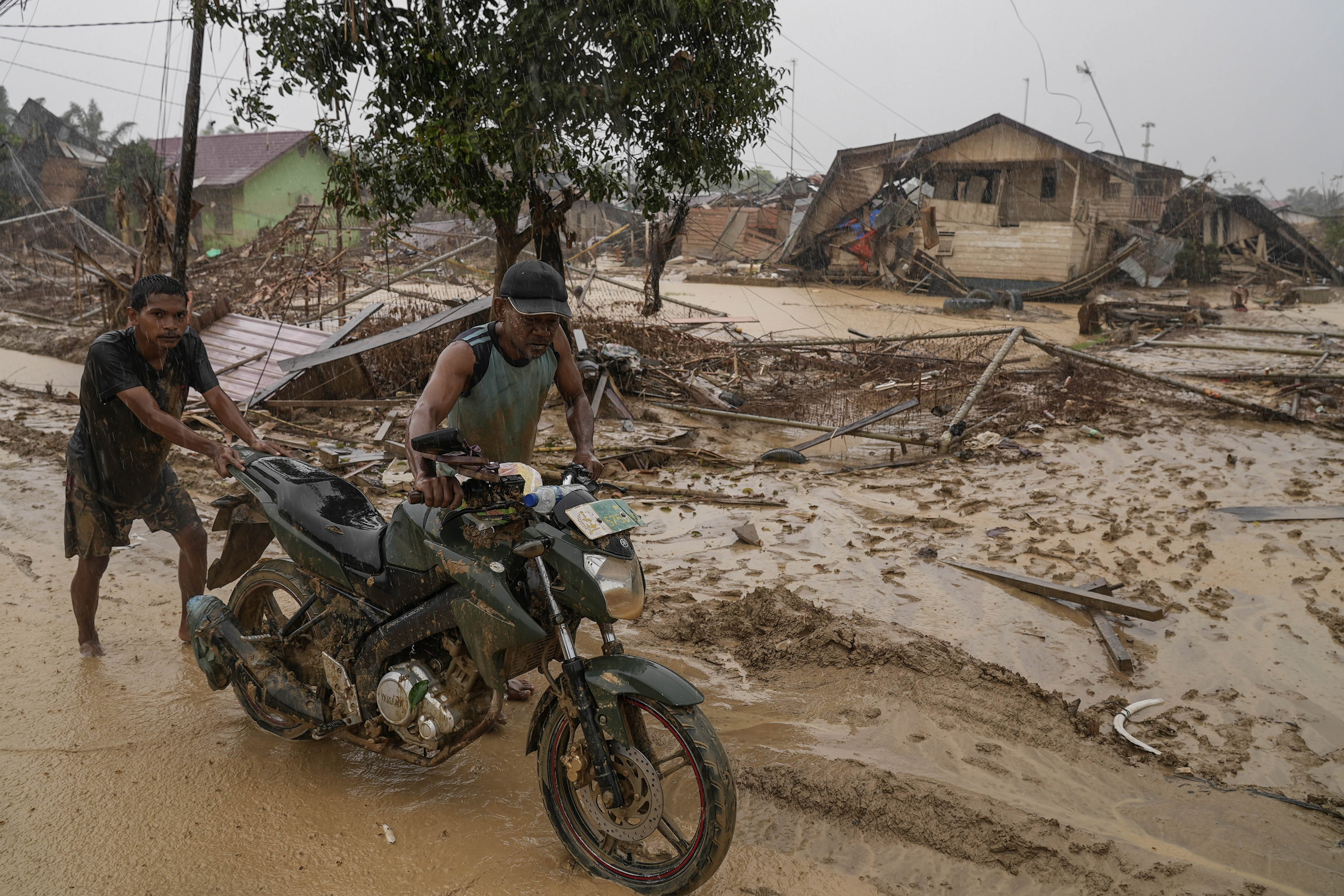 Warga mendorong sepeda motor melintas di desa yang luluh lantak pascabanjir di Desa Bundar, Karang Baru, Kabupaten Aceh Tamiang, Aceh, Selasa (9/12/2025). Badan Nasional Penanggulangan Bencana (BNPB) mencatat per Selasa (9/12) sebanyak 964 orang meninggal dan 264 jiwa belum ditemukan dengan rincian 31 jiwa masih hilang di Aceh, 138 jiwa hilang di Sumatera Utara, dan 95 hilang di Sumatera Barat.