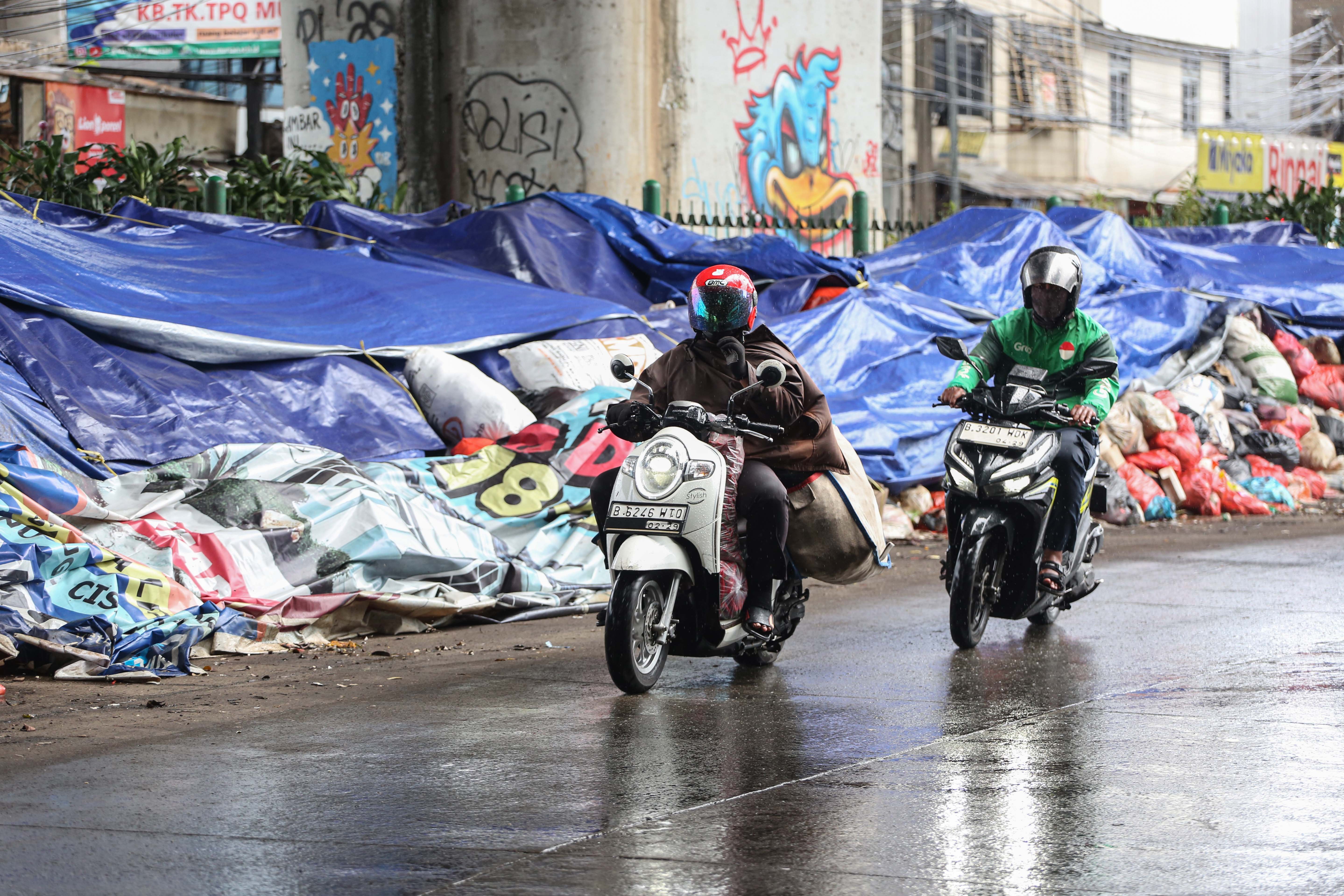 Pengendara sepeda motor melintas di dekat tumpukan sampah yang ditutupi terpal di Jalan Dewi Sartika, Ciputat, Kota Tangerang Selatan, Banten, Rabu (17/12/2025). Tumpukan sampah itu terjadi setelah Tempat Pembuangan Akhir (TPA) Cipeucang ditutup sementara dalam rangka perbaikan.