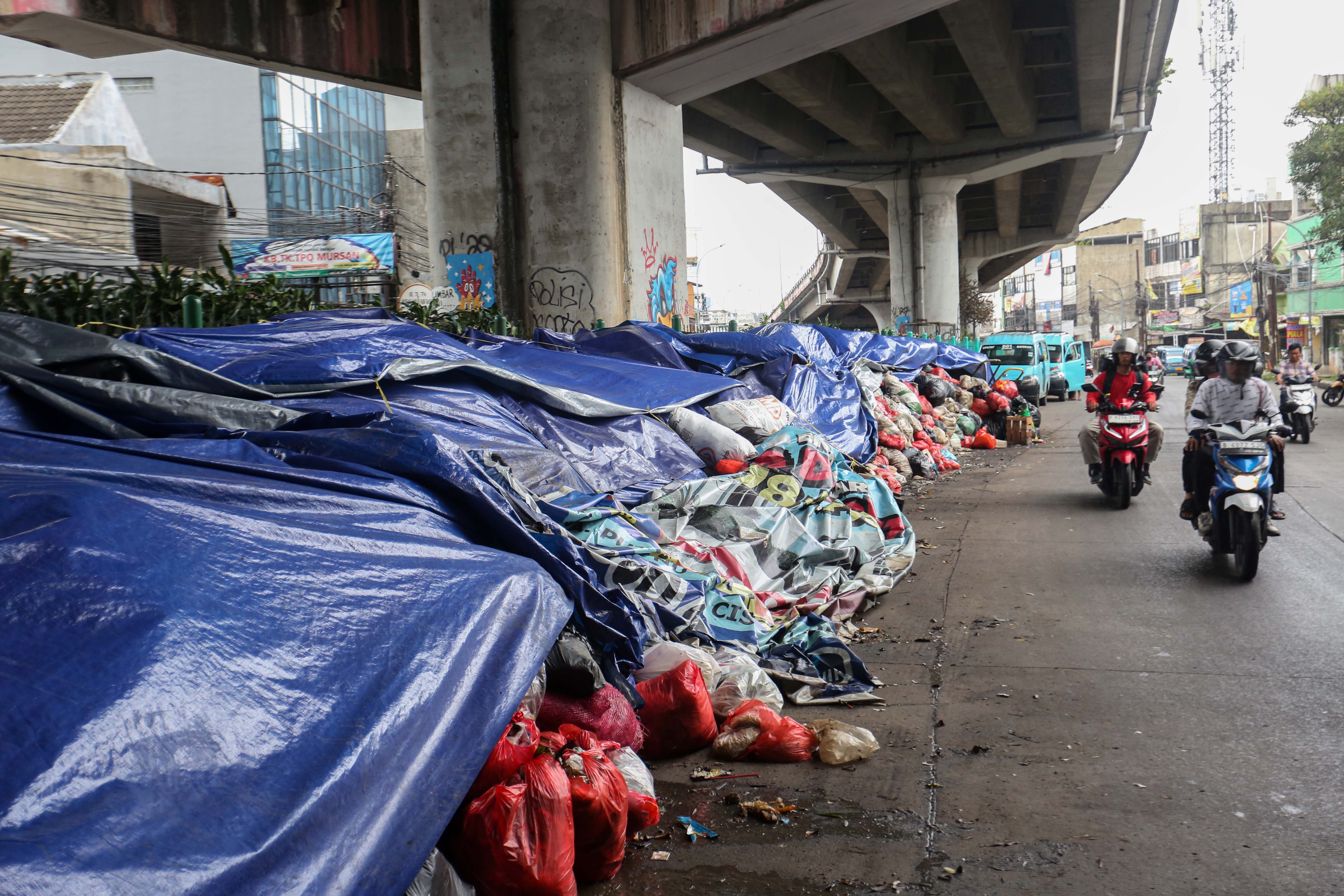 Pengendara sepeda motor melintas di dekat tumpukan sampah yang ditutupi terpal di Jalan Dewi Sartika, Ciputat, Kota Tangerang Selatan, Banten, Rabu (17/12/2025). Tumpukan sampah itu terjadi setelah Tempat Pembuangan Akhir (TPA) Cipeucang ditutup sementara dalam rangka perbaikan.