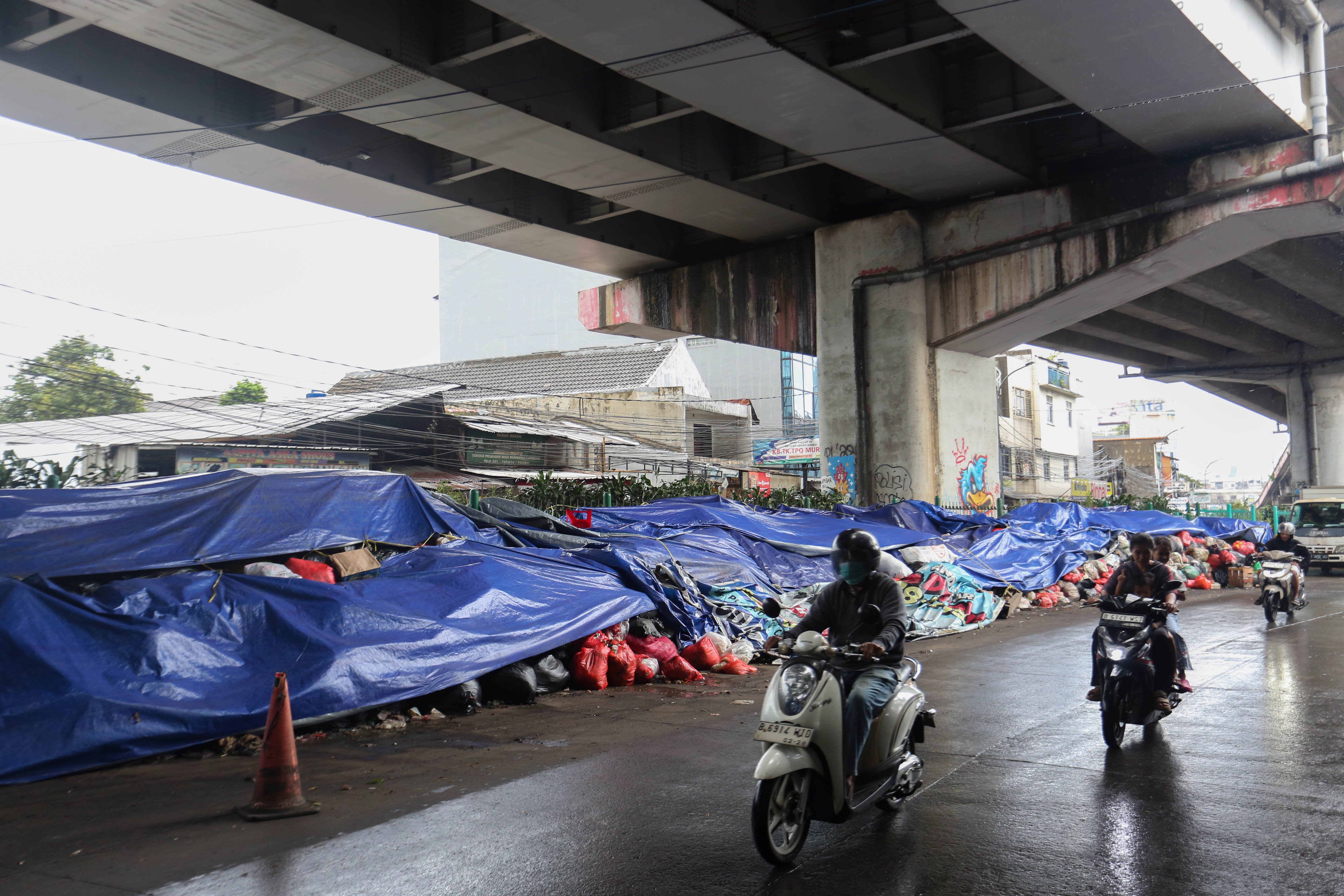 Pengendara sepeda motor melintas di dekat tumpukan sampah yang ditutupi terpal di Jalan Dewi Sartika, Ciputat, Kota Tangerang Selatan, Banten, Rabu (17/12/2025). Tumpukan sampah itu terjadi setelah Tempat Pembuangan Akhir (TPA) Cipeucang ditutup sementara dalam rangka perbaikan.