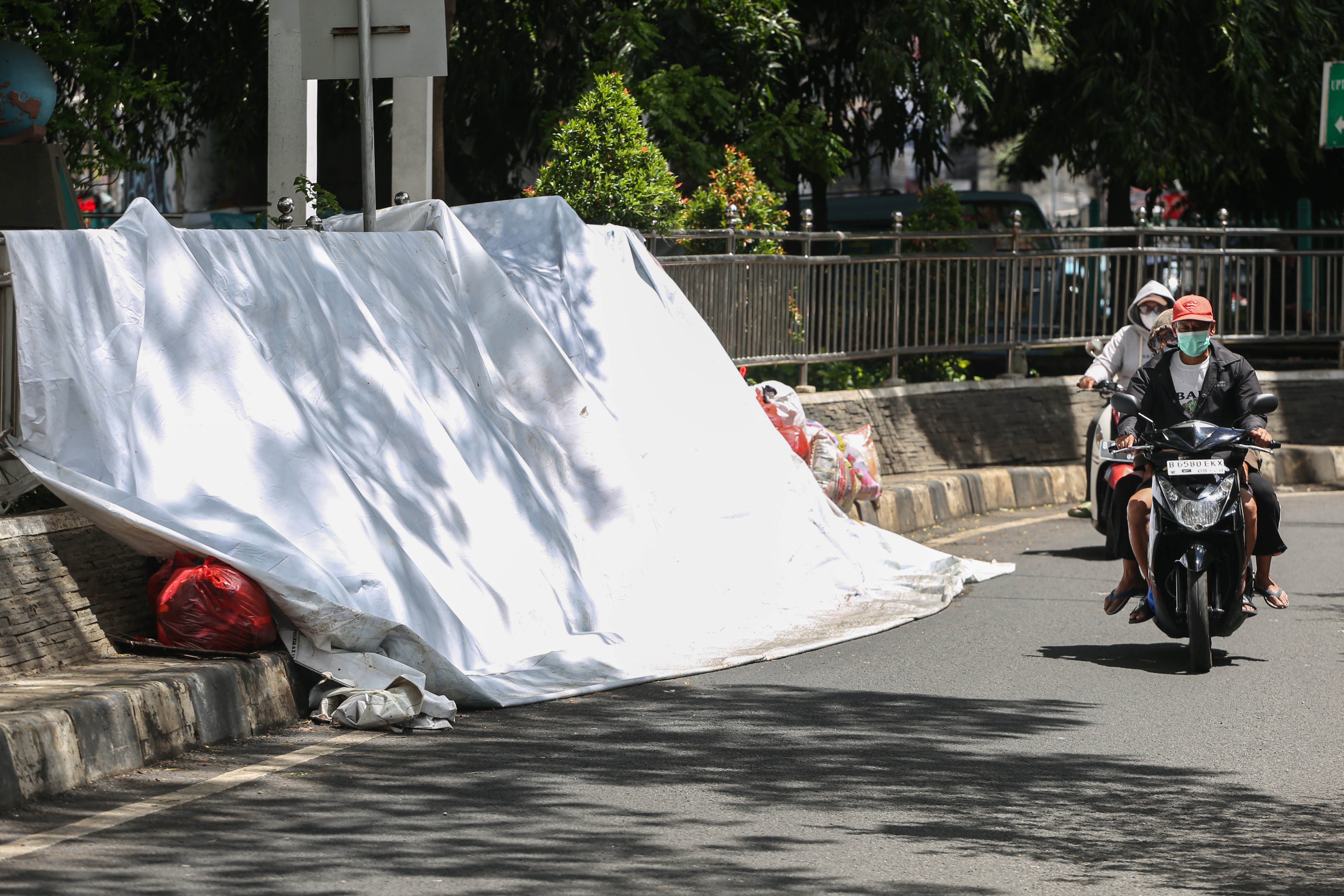 Pengendara sepeda motor melintas di dekat tumpukan sampah yang ditutupi terpal di Jalan Dewi Sartika, Ciputat, Kota Tangerang Selatan, Banten, Rabu (17/12/2025). Tumpukan sampah itu terjadi setelah Tempat Pembuangan Akhir (TPA) Cipeucang ditutup sementara dalam rangka perbaikan.