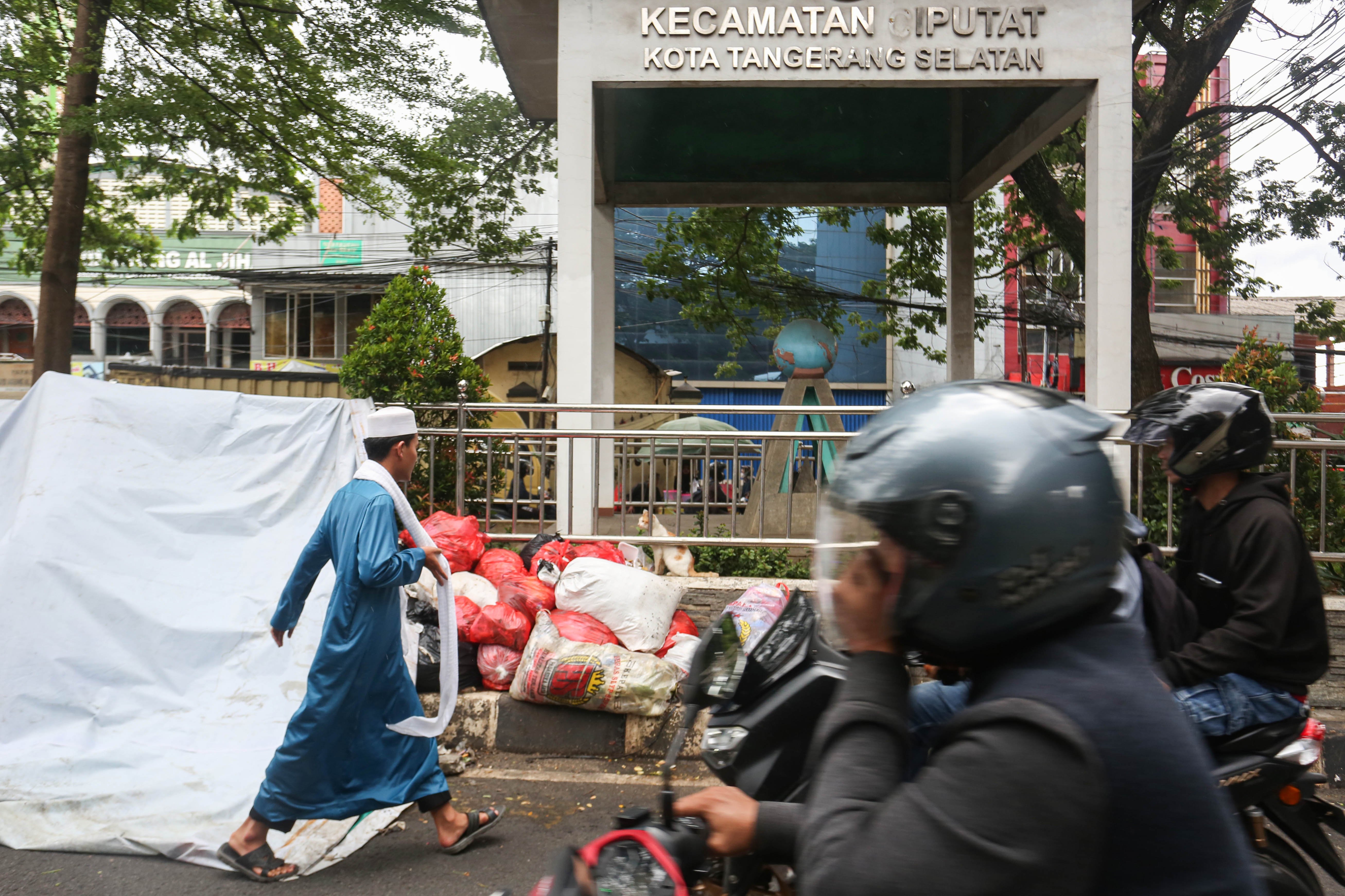 Seorang warga dan pengendara sepeda motor melintas di dekat tumpukan sampah yang ditutupi terpal di Jalan Dewi Sartika, Ciputat, Kota Tangerang Selatan, Banten, Rabu (17/12/2025). Tumpukan sampah itu terjadi setelah Tempat Pembuangan Akhir (TPA) Cipeucang ditutup sementara dalam rangka perbaikan.