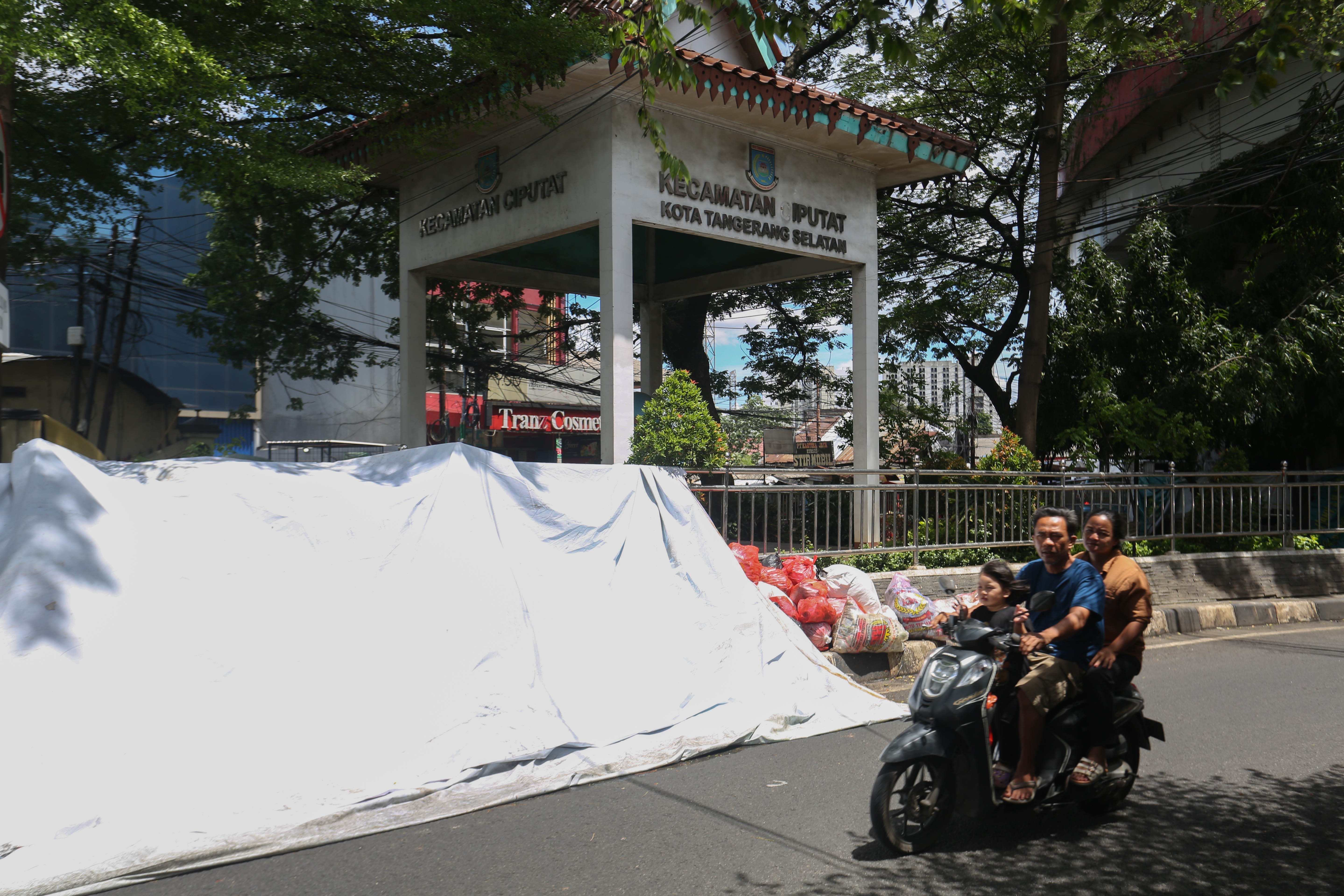 Pengendara sepeda motor melintas di dekat tumpukan sampah yang ditutupi terpal di Jalan Dewi Sartika, Ciputat, Kota Tangerang Selatan, Banten, Rabu (17/12/2025). Tumpukan sampah itu terjadi setelah Tempat Pembuangan Akhir (TPA) Cipeucang ditutup sementara dalam rangka perbaikan.