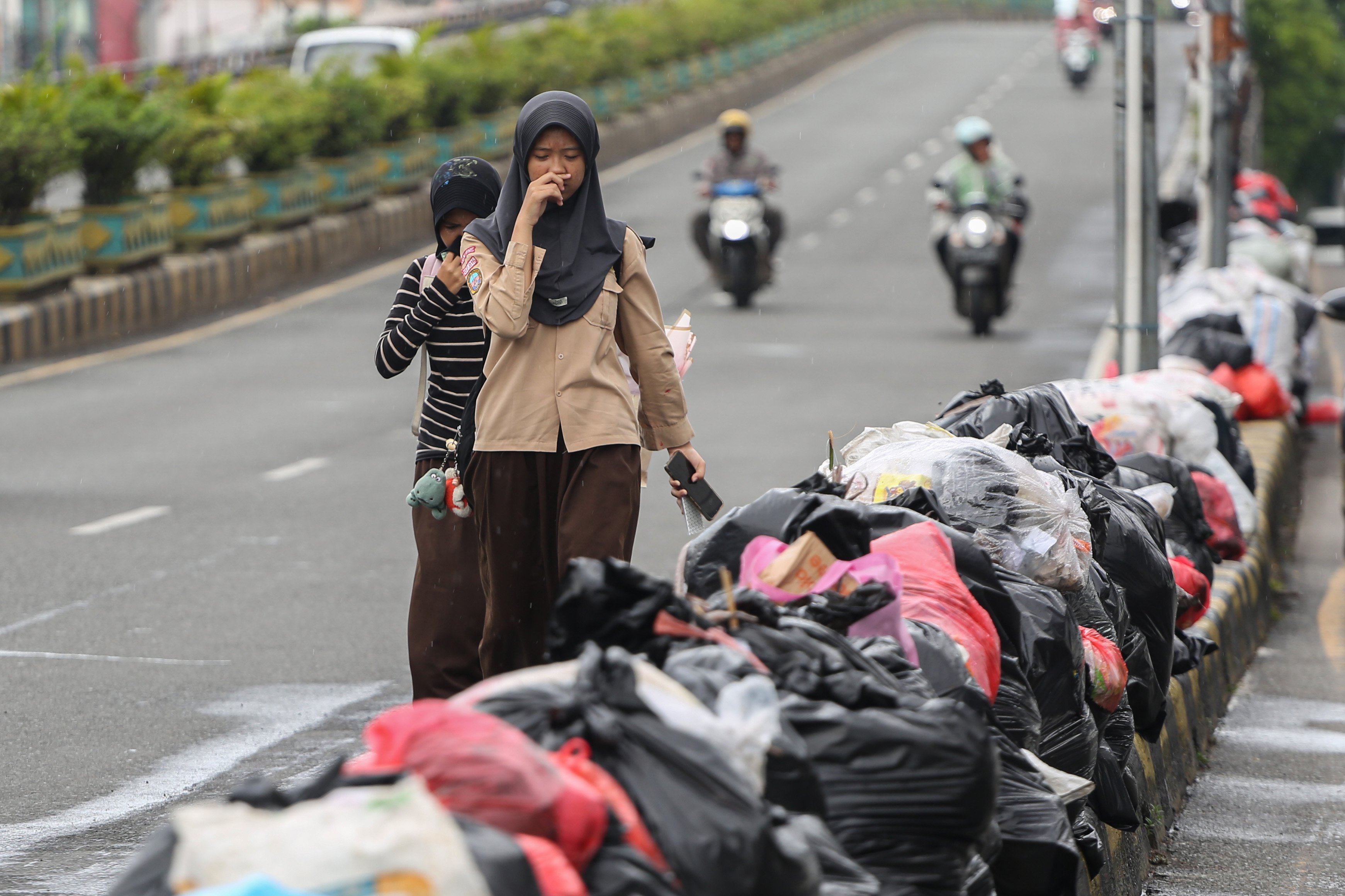 Siswa sekolah menutup hidungnya saat berjalan di dekat tumpukan sampah di Jalan Dewi Sartika, Ciputat, Kota Tangerang Selatan, Banten, Rabu (17/12/2025). Tumpukan sampah itu terjadi setelah Tempat Pembuangan Akhir (TPA) Cipeucang ditutup sementara dalam rangka perbaikan.