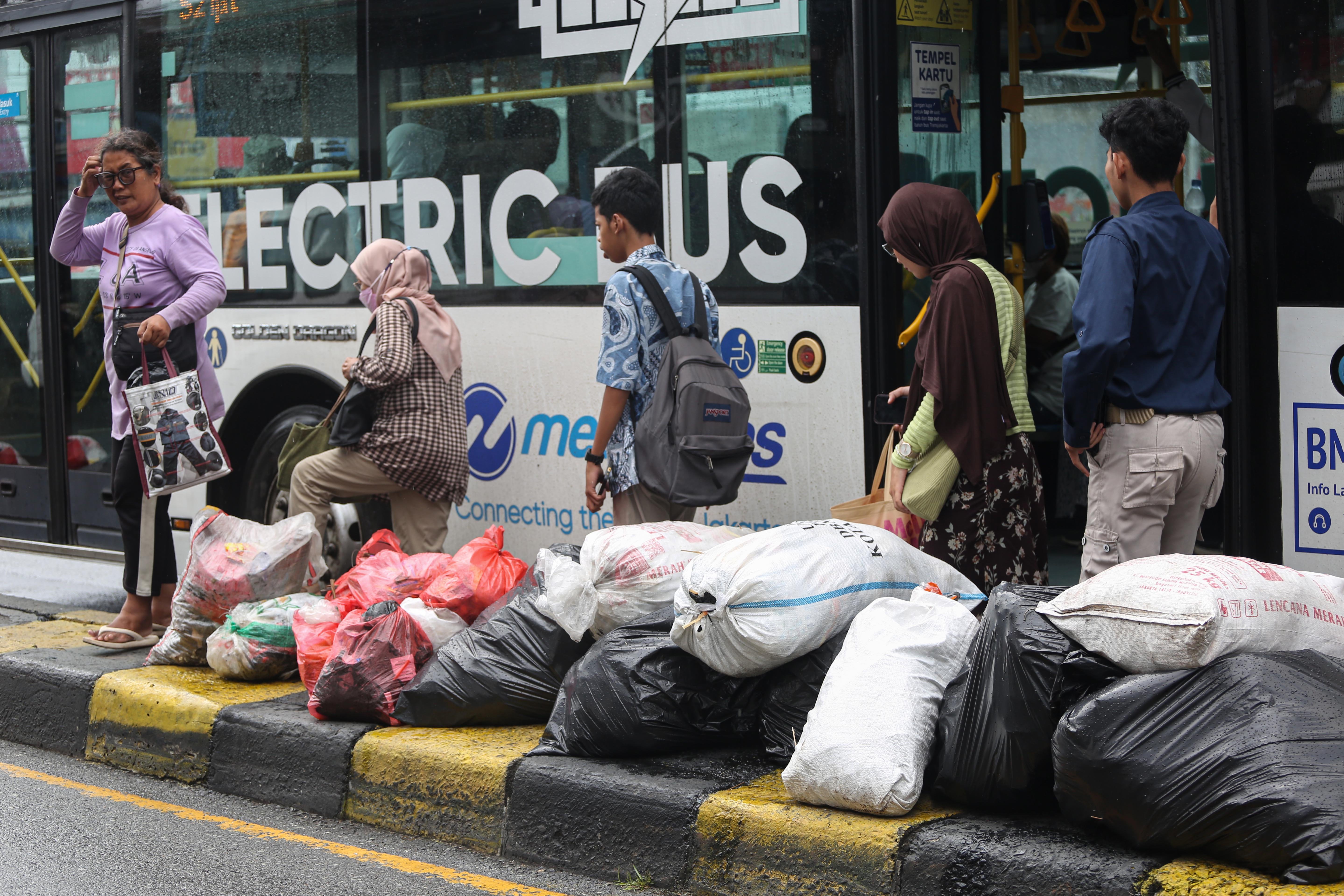Warga berada di dekat tumpukan sampah setelah turun dari bus Transjakarta di Jalan Dewi Sartika, Ciputat, Kota Tangerang Selatan, Banten, Rabu (17/12/2025). Tumpukan sampah itu terjadi setelah Tempat Pembuangan Akhir (TPA) Cipeucang ditutup sementara dalam rangka perbaikan.