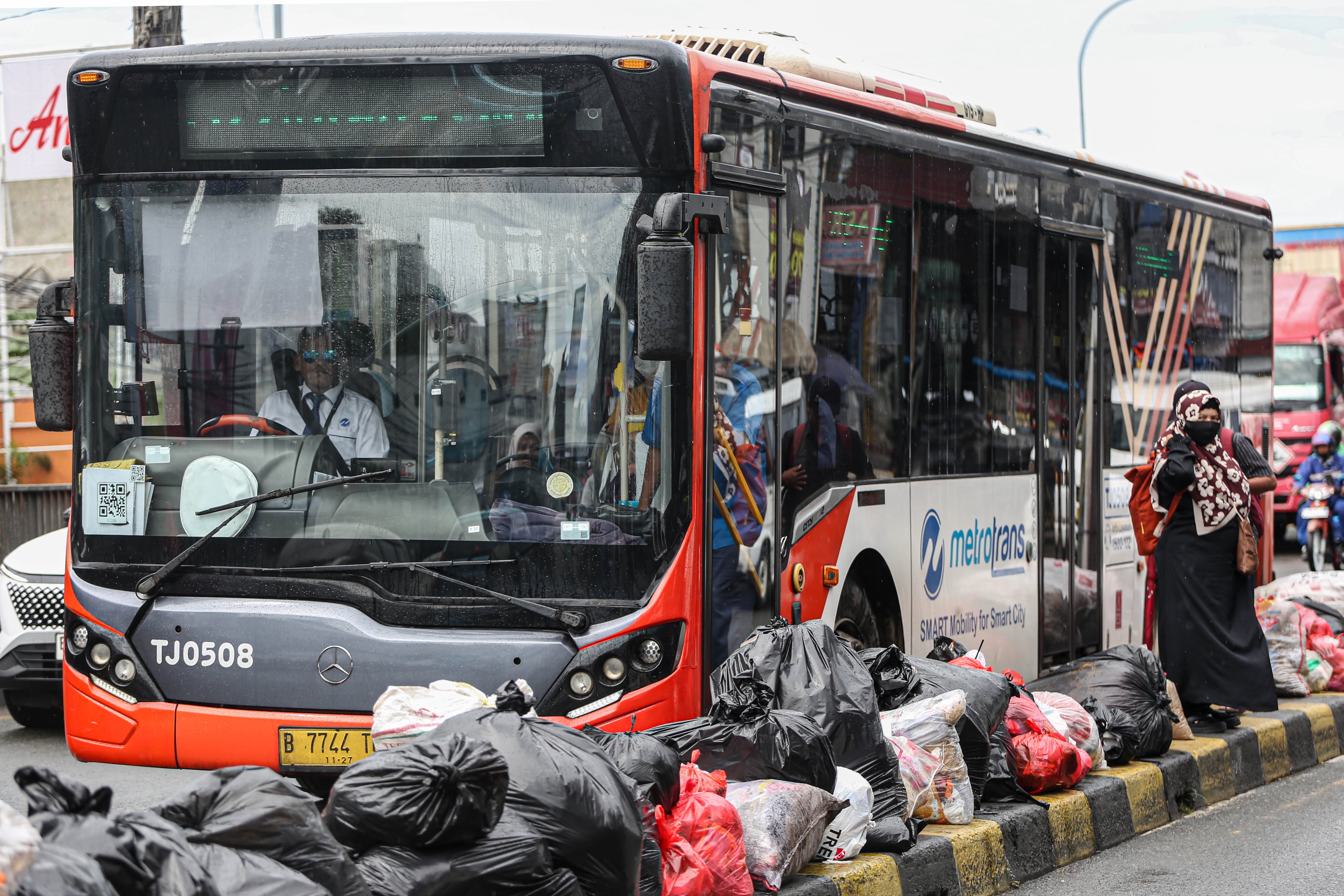 Warga berada di dekat tumpukan sampah setelah turun dari bus Transjakarta di Jalan Dewi Sartika, Ciputat, Kota Tangerang Selatan, Banten, Rabu (17/12/2025). Tumpukan sampah itu terjadi setelah Tempat Pembuangan Akhir (TPA) Cipeucang ditutup sementara dalam rangka perbaikan.