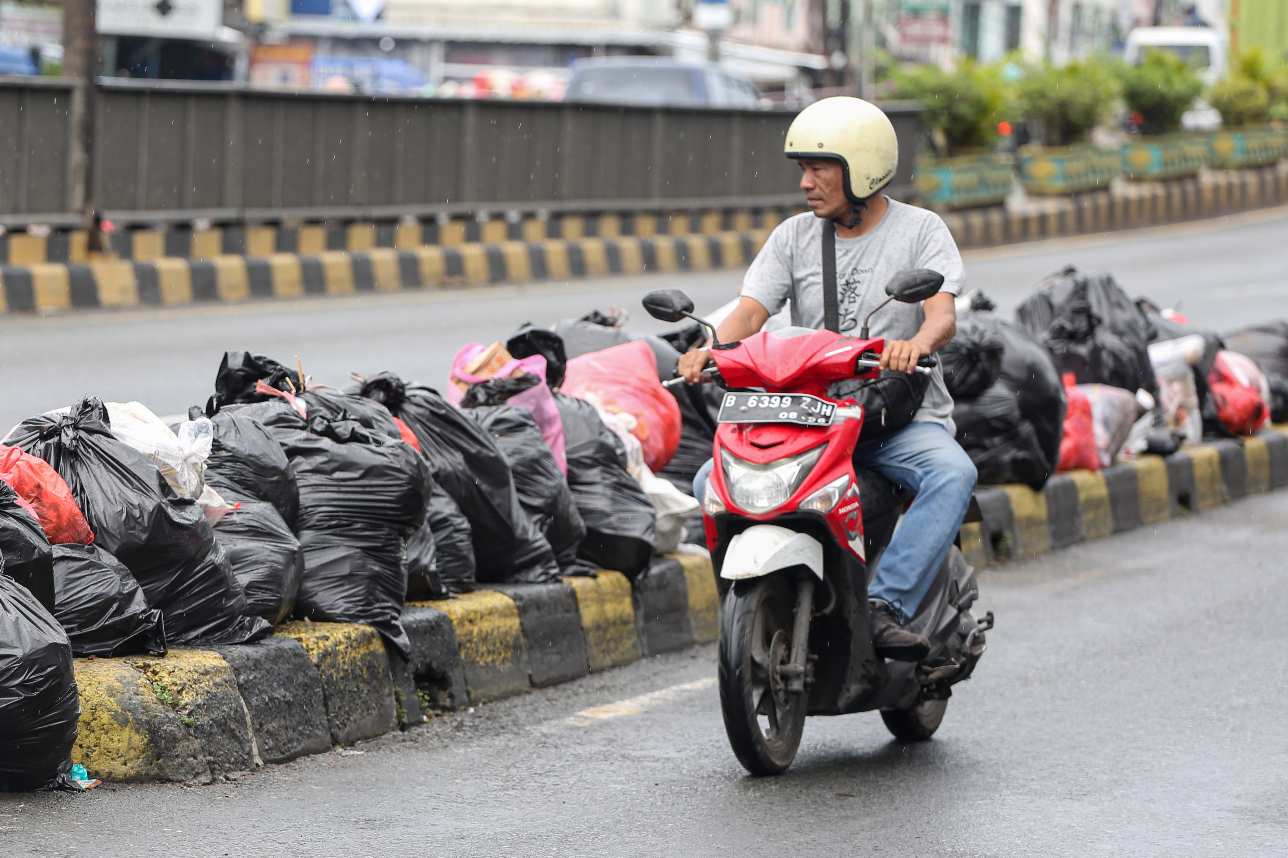 Pengendara sepeda motor melintas di dekat tumpukan sampah di Jalan Dewi Sartika, Ciputat, Kota Tangerang Selatan, Banten, Rabu (17/12/2025). Tumpukan sampah itu terjadi setelah Tempat Pembuangan Akhir (TPA) Cipeucang ditutup sementara dalam rangka perbaikan.