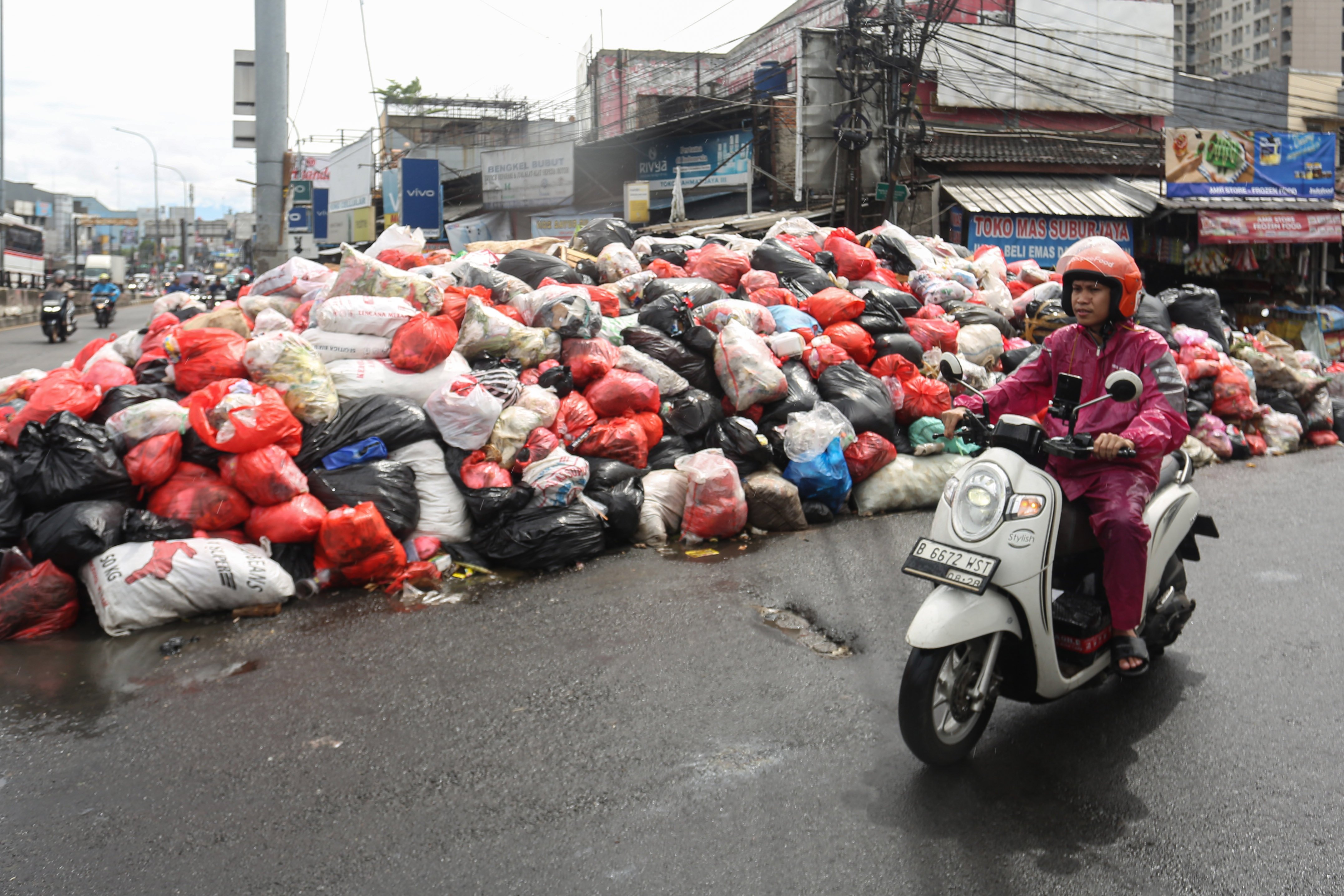 Pengendara sepeda motor melintas di dekat tumpukan sampah di Jalan Dewi Sartika, Ciputat, Kota Tangerang Selatan, Banten, Rabu (17/12/2025). Tumpukan sampah itu terjadi setelah Tempat Pembuangan Akhir (TPA) Cipeucang ditutup sementara dalam rangka perbaikan.