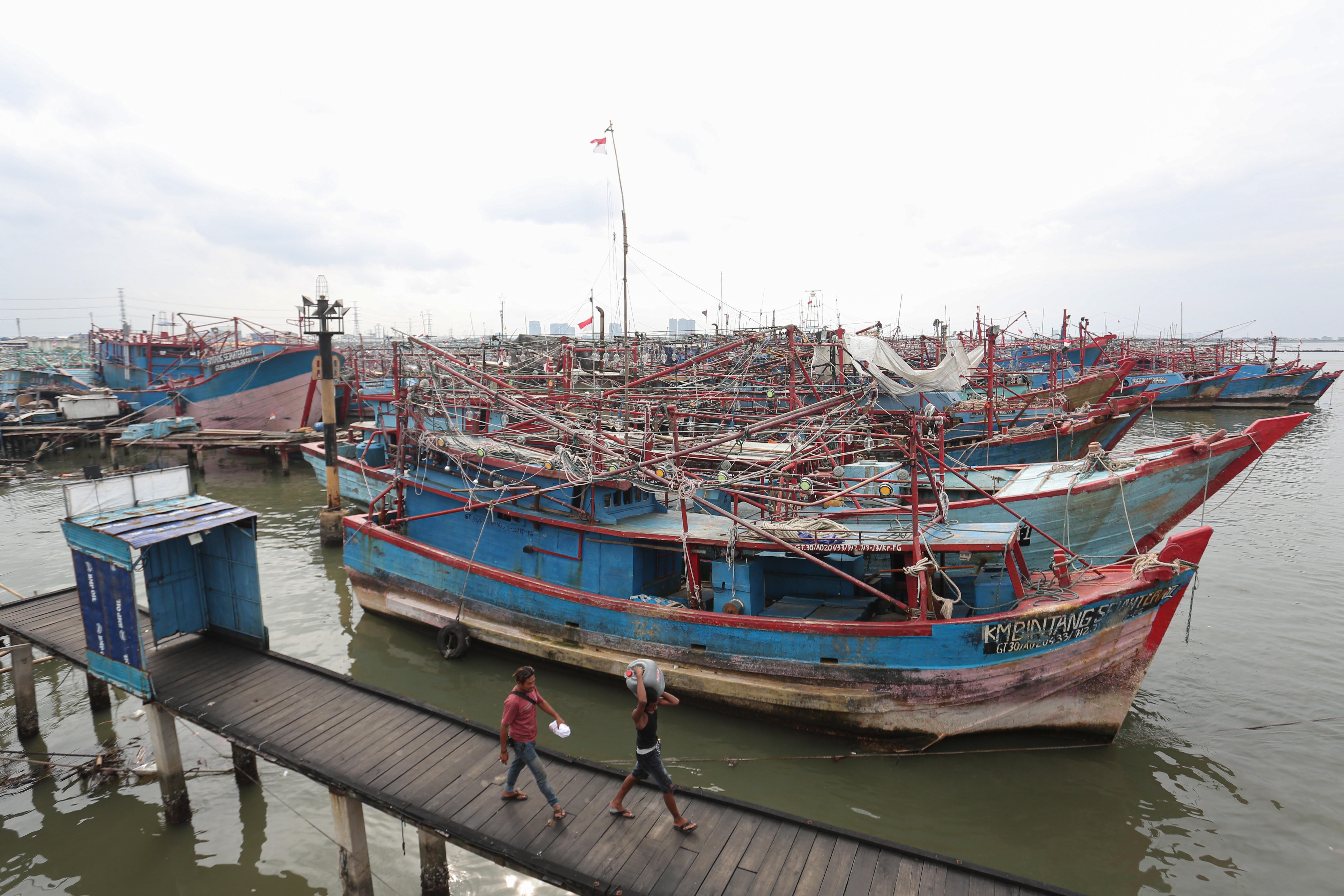 Warga berjalan di samping kapal kapal nelayan yang menumpuk saat bersandar di Pelabuhan Perikanan Nusantara (PPN) Muara Angke, Jakarta Utara, Senin (9/2/2026). Kadatan kapal tersebut terjadi karena kondisi cuaca buruk yang membuat kapal tidak melaut hingga menumpuk dan melebihi kapasitas kolam. 