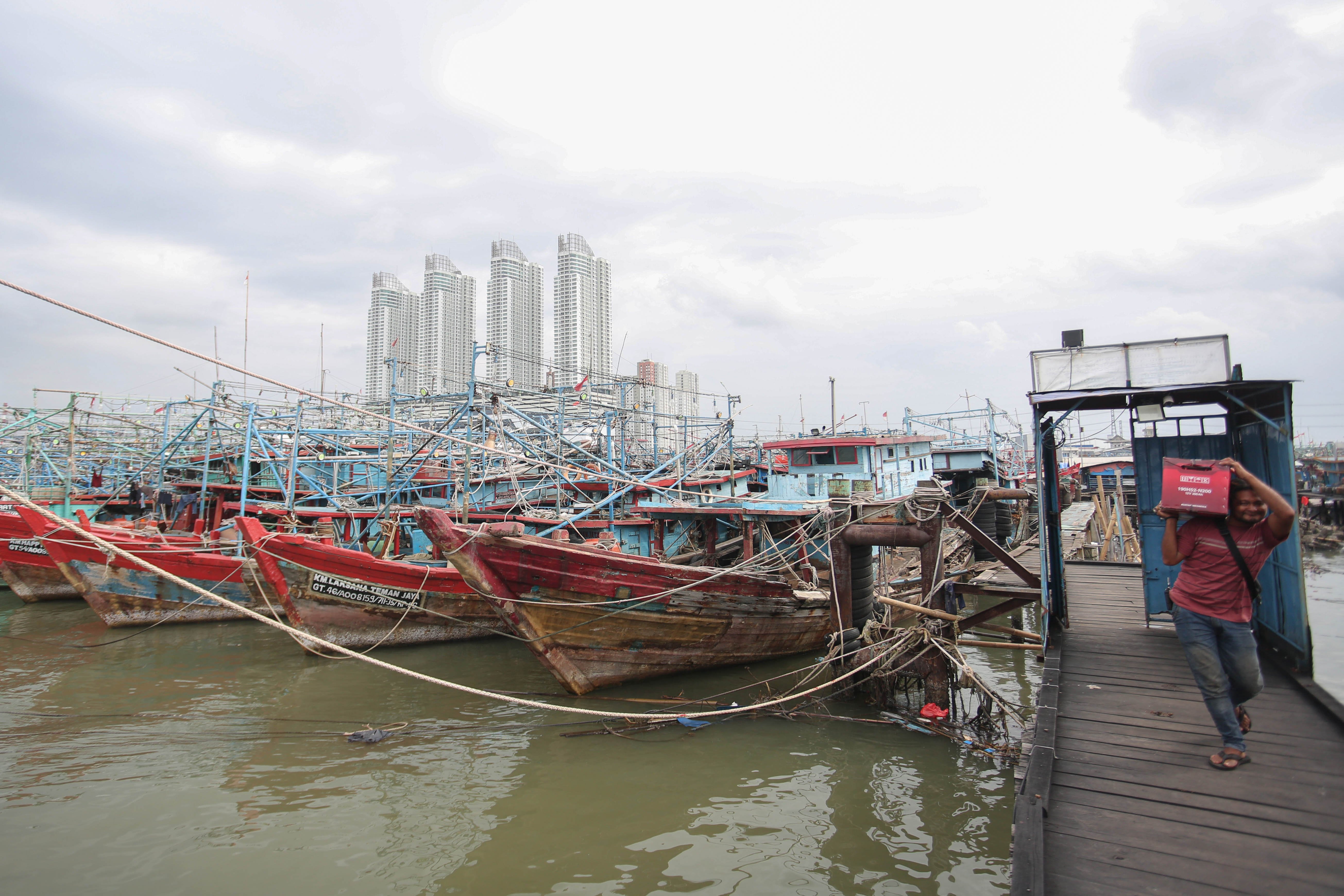 Warga berjalan di samping kapal kapal nelayan yang menumpuk saat bersandar di Pelabuhan Perikanan Nusantara (PPN) Muara Angke, Jakarta Utara, Senin (9/2/2026). Kadatan kapal tersebut terjadi karena kondisi cuaca buruk yang membuat kapal tidak melaut hingga menumpuk dan melebihi kapasitas kolam. 