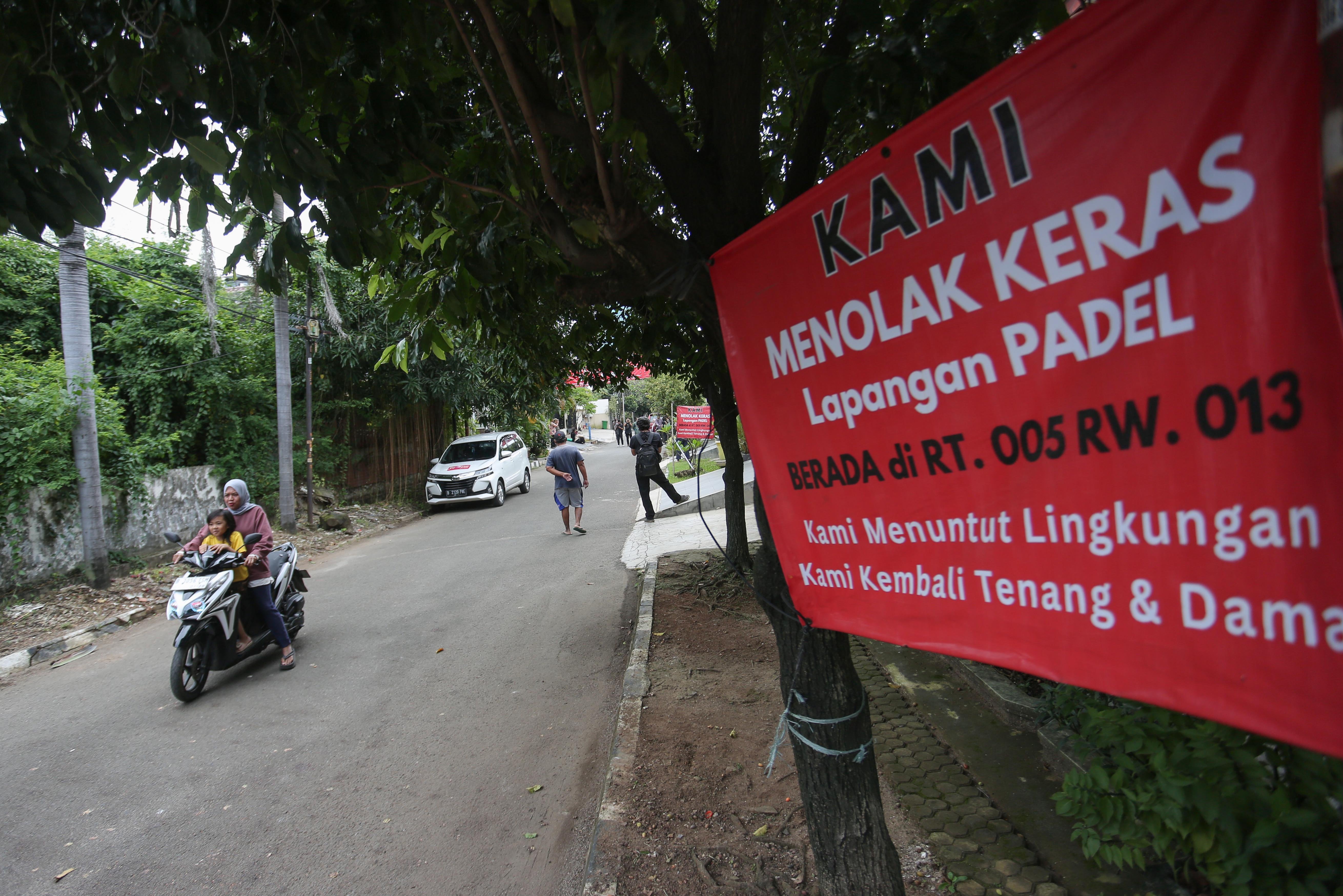 Pengendara sepeda motor melintas di dekat spanduk penolakan lapangan padel di kawasan perumahan, Jalan Pulomas Barat II, Kayu Putih, Pulogadung, Jakarta Timur, Kamis (26/2/2026). Berdasarkan penuturan warga aksi pemasangan spanduk tersebut sebagai bentuk protes terhadap aktivitas olahraga di lapangan padel yang kerap menimbulkan suara bising dan mengganggu ketenangan warga.