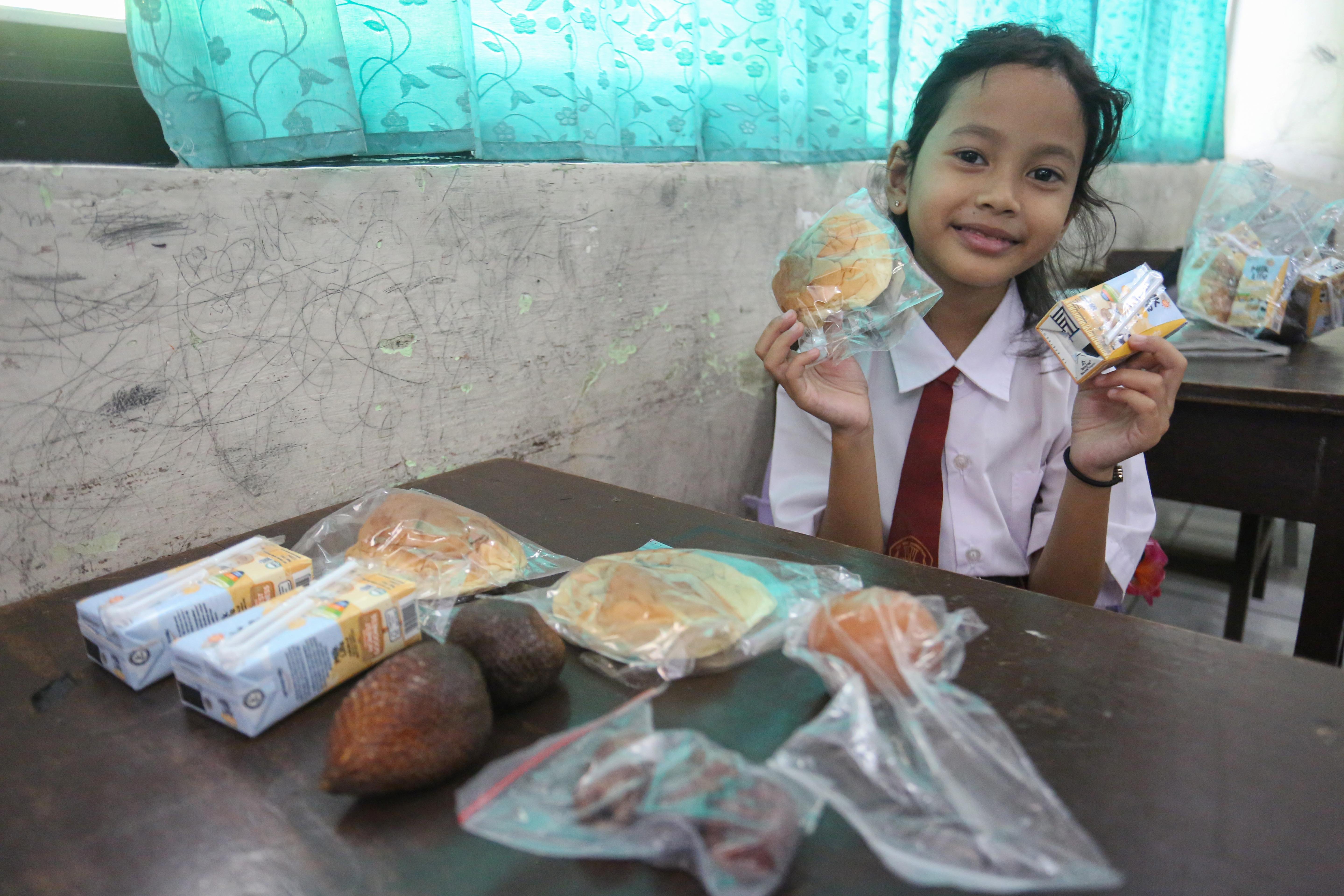 Siswi menunjukkan makanan pada paket Makan Bergizi Gratis (MBG) yang dibagikan di SDN Slipi 15, Jakarta, Senin (2/3/2026). Pada bulan Ramadan siswa mendapatkan MBG untuk dimakan di rumah saat berbuka puasa dengan menu yang terdiri dari roti, buah salak, kurma, telur rebus, kacang pilus dan susu kemasan.