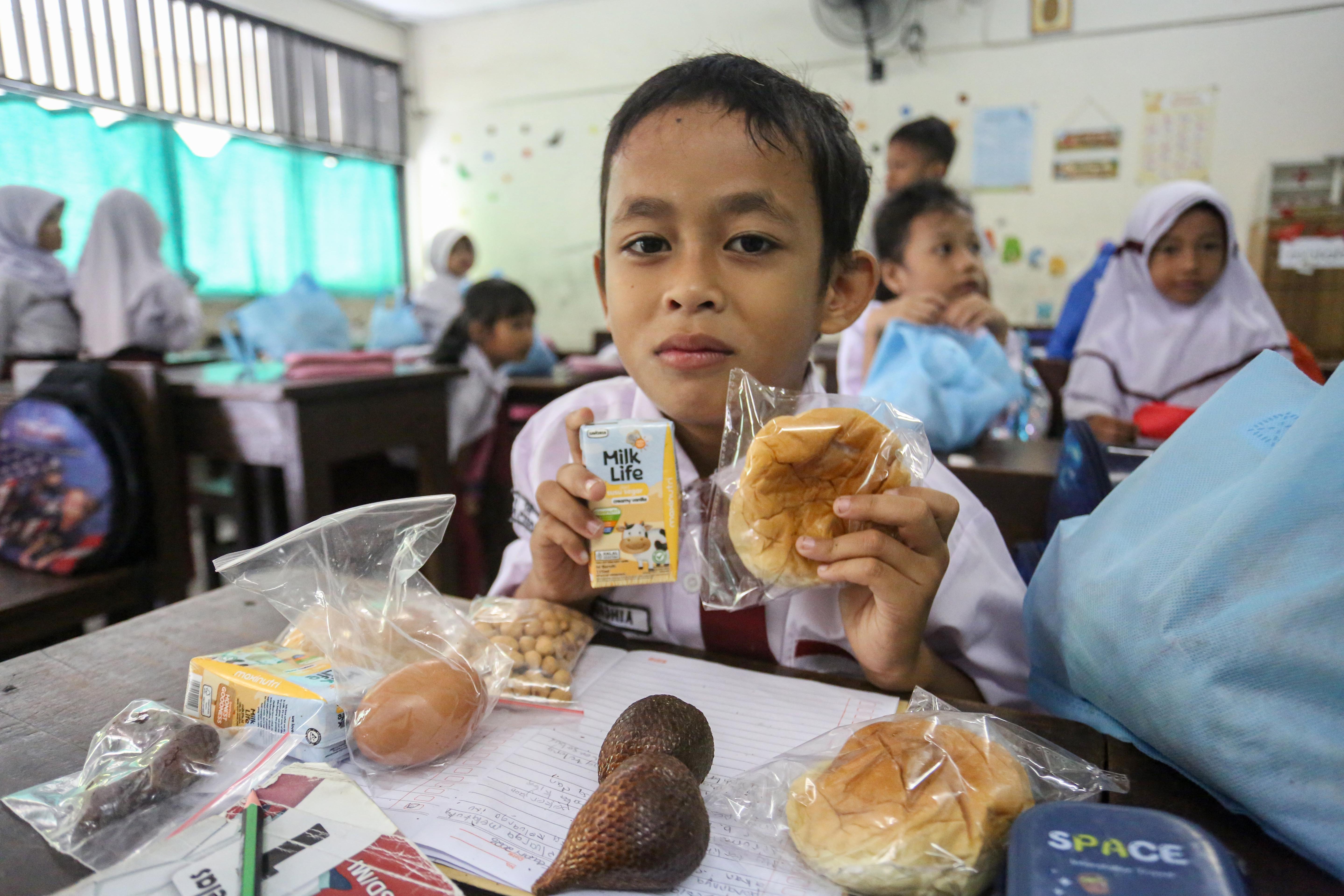 Siswa menunjukkan makanan pada paket Makan Bergizi Gratis (MBG) yang dibagikan di SDN Slipi 15, Jakarta, Senin (2/3/2026). Pada bulan Ramadan siswa mendapatkan MBG untuk dimakan di rumah saat berbuka puasa dengan menu yang terdiri dari roti, buah salak, kurma, telur rebus, kacang pilus dan susu kemasan.