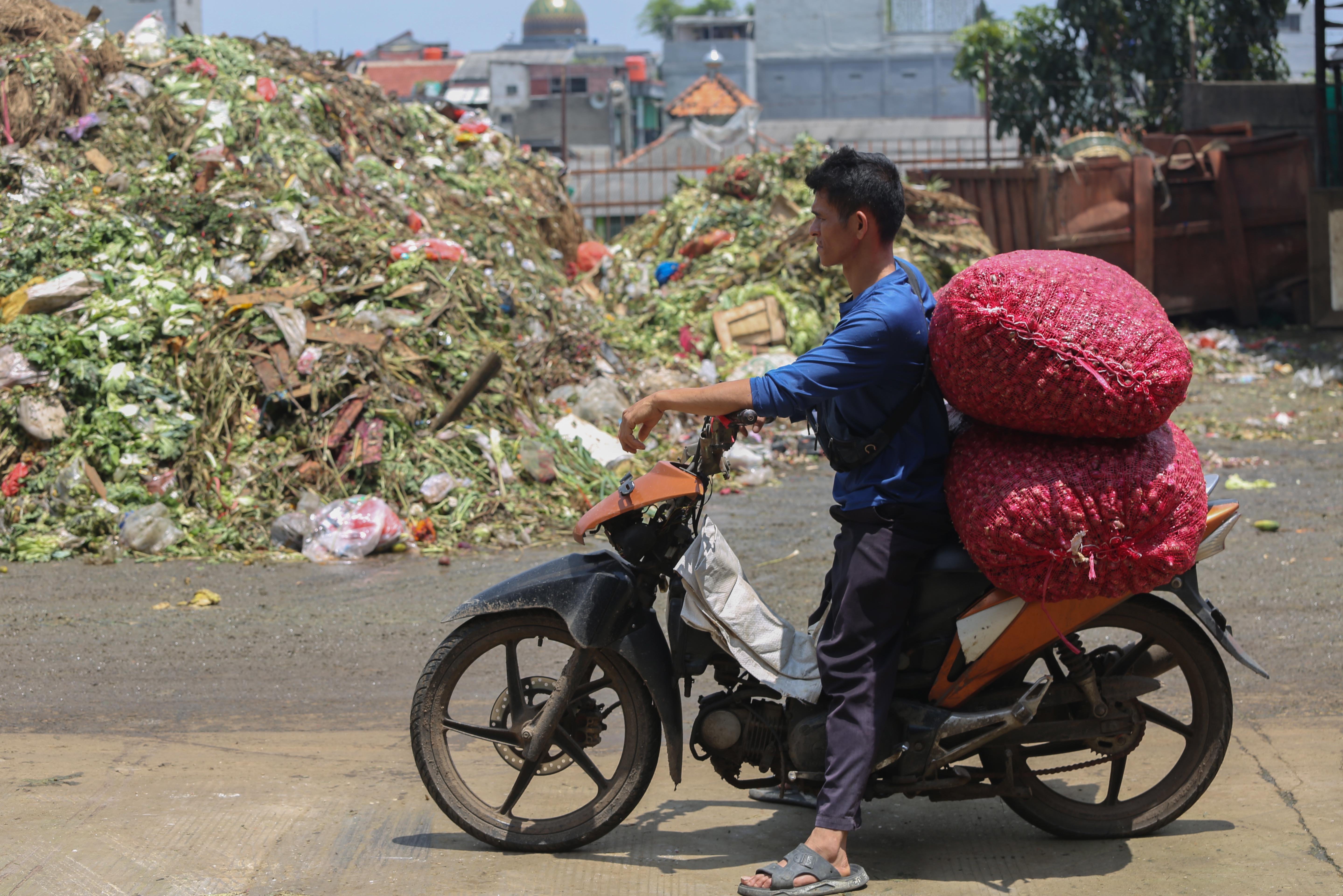 Pedagang yang mengangkut bawang merah melintas di dekat tumpukan sampah di Pasar Induk Kramat Jati, Jakarta Timur, Rabu (1/4/2026). Keterbatasan kuota pembuangan ke Tempat Pengolahan Sampah Terpadu (TPST) Bantar Gebang pascainsiden longsor yang terjadi membuat sampah menumpuk di Pasar Induk Kramat Jati.