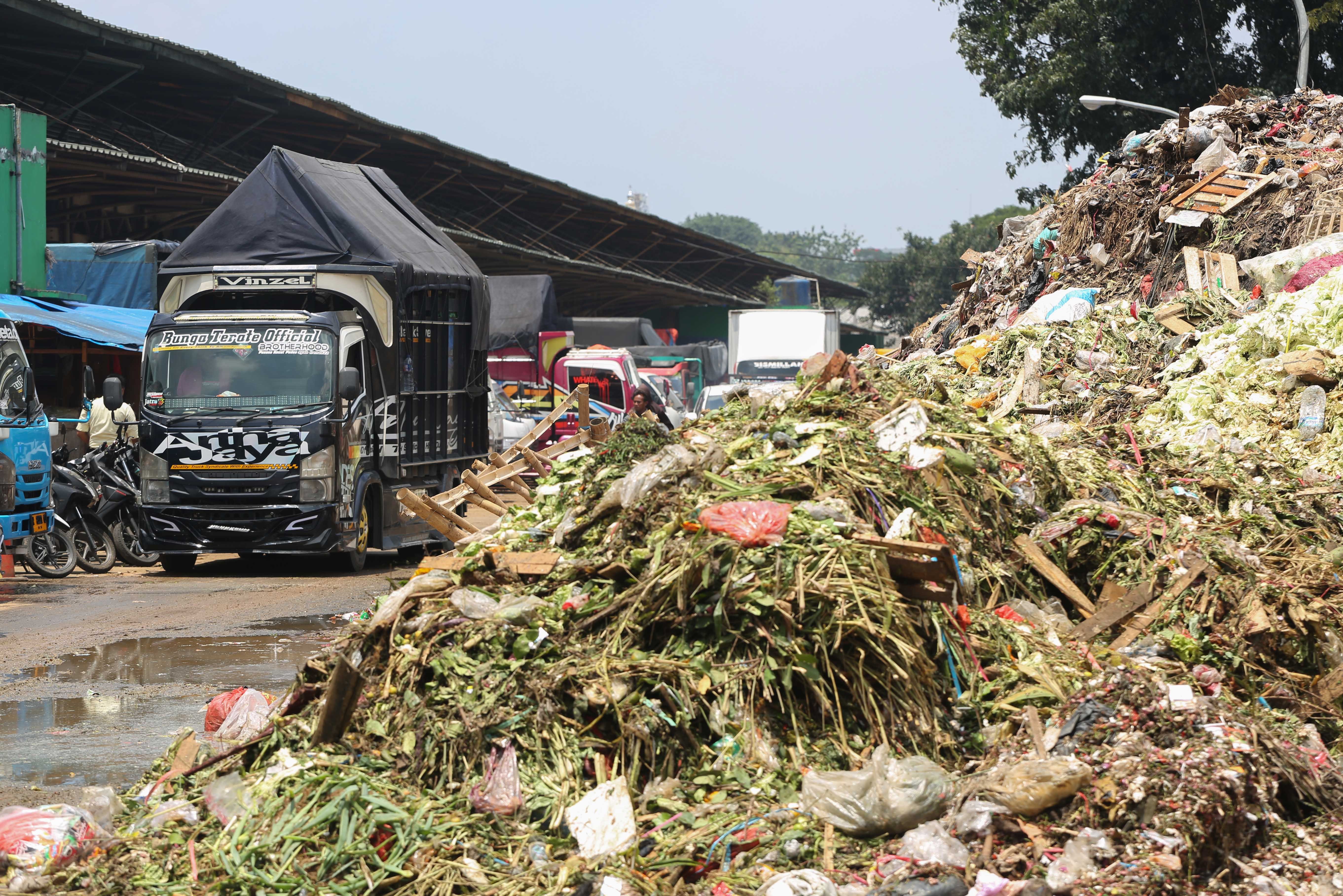 Truk melintas di dekat tumpukan sampah di Pasar Induk Kramat Jati, Jakarta Timur, Rabu (1/4/2026). Keterbatasan kuota pembuangan ke Tempat Pengolahan Sampah Terpadu (TPST) Bantar Gebang pascainsiden longsor yang terjadi membuat sampah menumpuk di Pasar Induk Kramat Jati.
