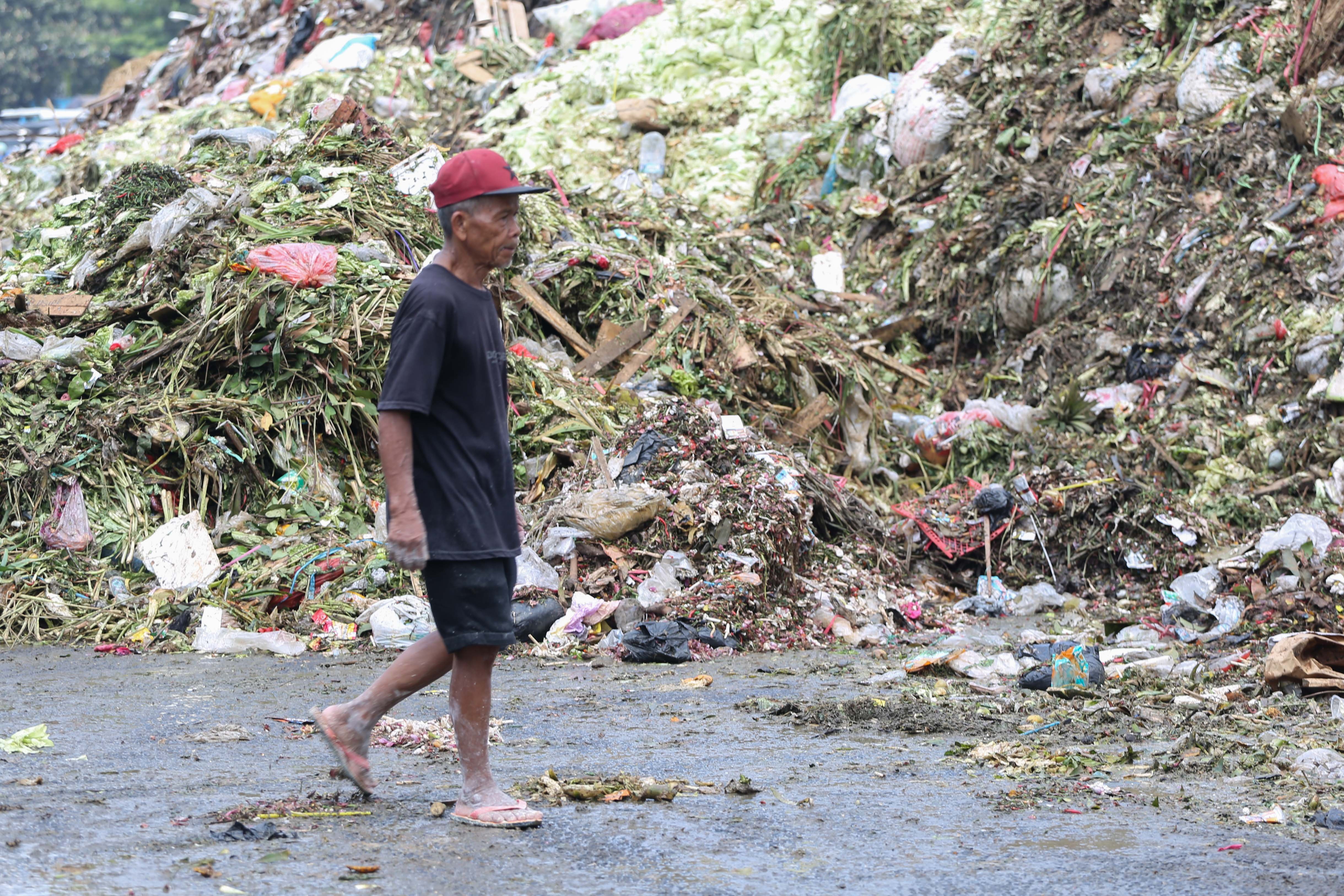 Warga berjalan di dekat tumpukan sampah di Pasar Induk Kramat Jati, Jakarta Timur, Rabu (1/4/2026). Keterbatasan kuota pembuangan ke Tempat Pengolahan Sampah Terpadu (TPST) Bantar Gebang pascainsiden longsor yang terjadi membuat sampah menumpuk di Pasar Induk Kramat Jati.