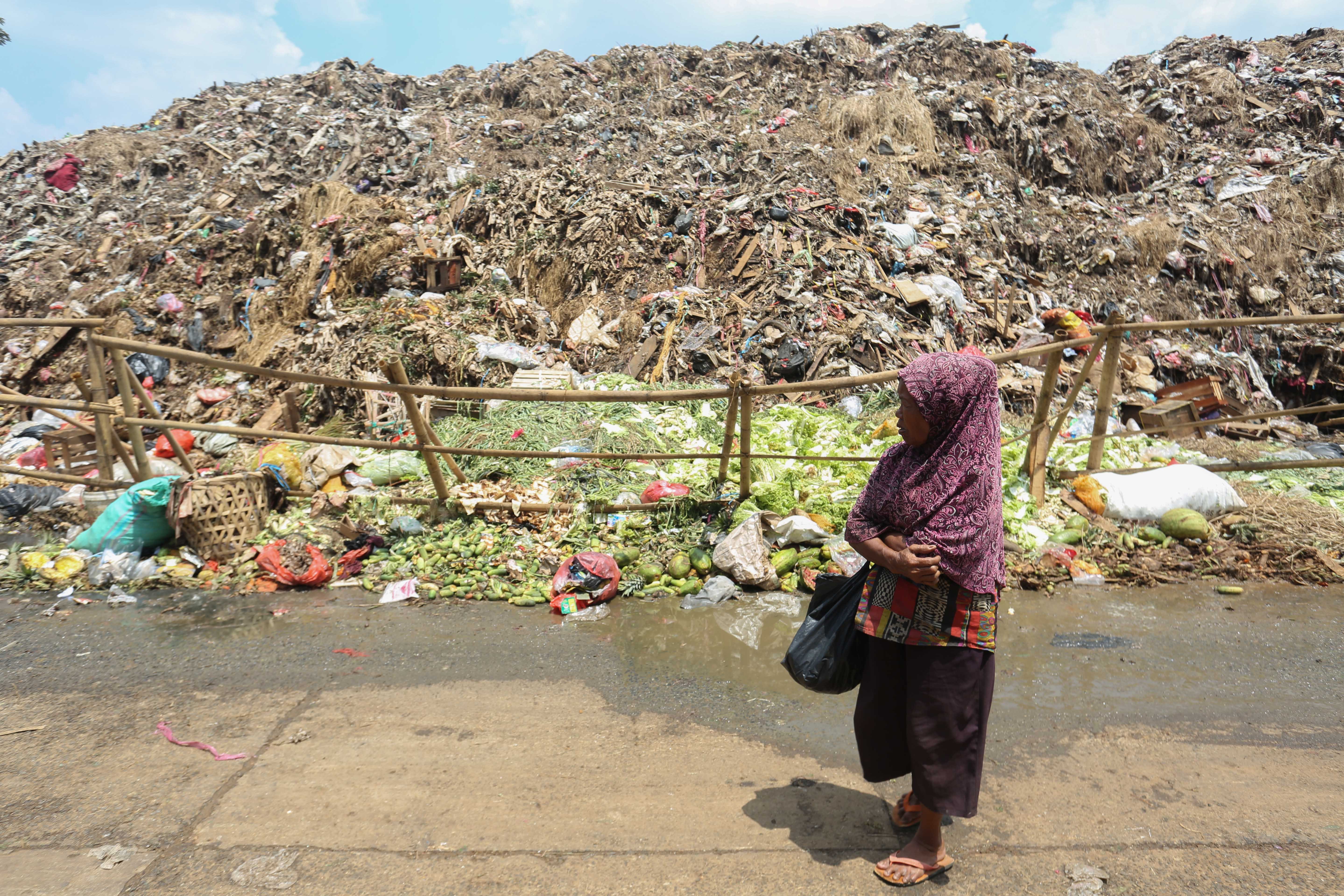 Warga berjalan di dekat tumpukan sampah di Pasar Induk Kramat Jati, Jakarta Timur, Rabu (1/4/2026). Keterbatasan kuota pembuangan ke Tempat Pengolahan Sampah Terpadu (TPST) Bantar Gebang pascainsiden longsor yang terjadi membuat sampah menumpuk di Pasar Induk Kramat Jati.