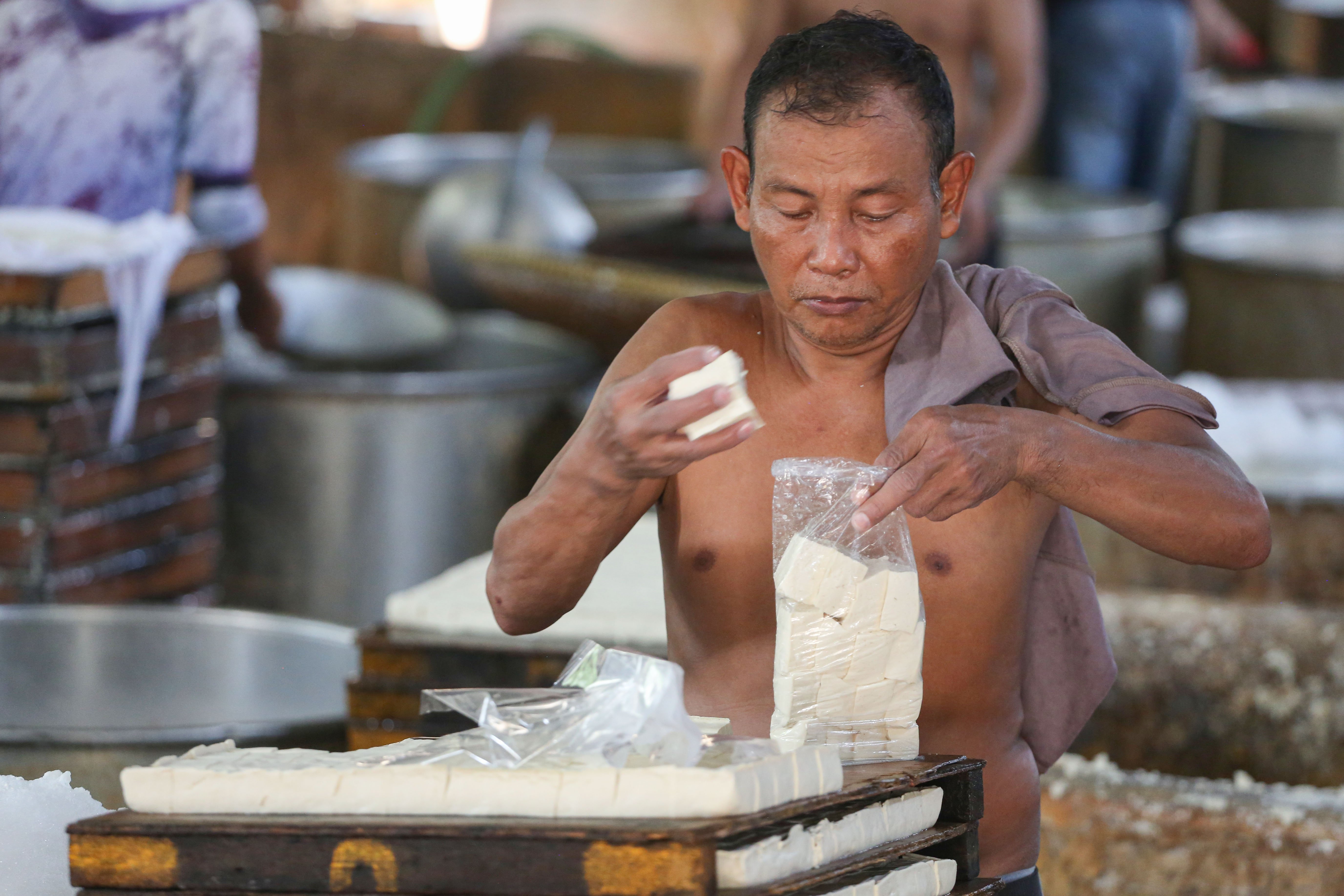 Pekerja mengemas tahu ke dalam plastik di rumah produksi tahu kawasan Duren Tiga, Jakarta, Senin (13/4/2026). Kenaikan harga kedelai dari Rp 8.600 hingga Rp 11.000 per kilogramnya membuat pengrajin mengurangi ukuran tahu guna mencegah kenaikan harga jual ke pasar sehingga daya beli konsumen dapat terjaga.