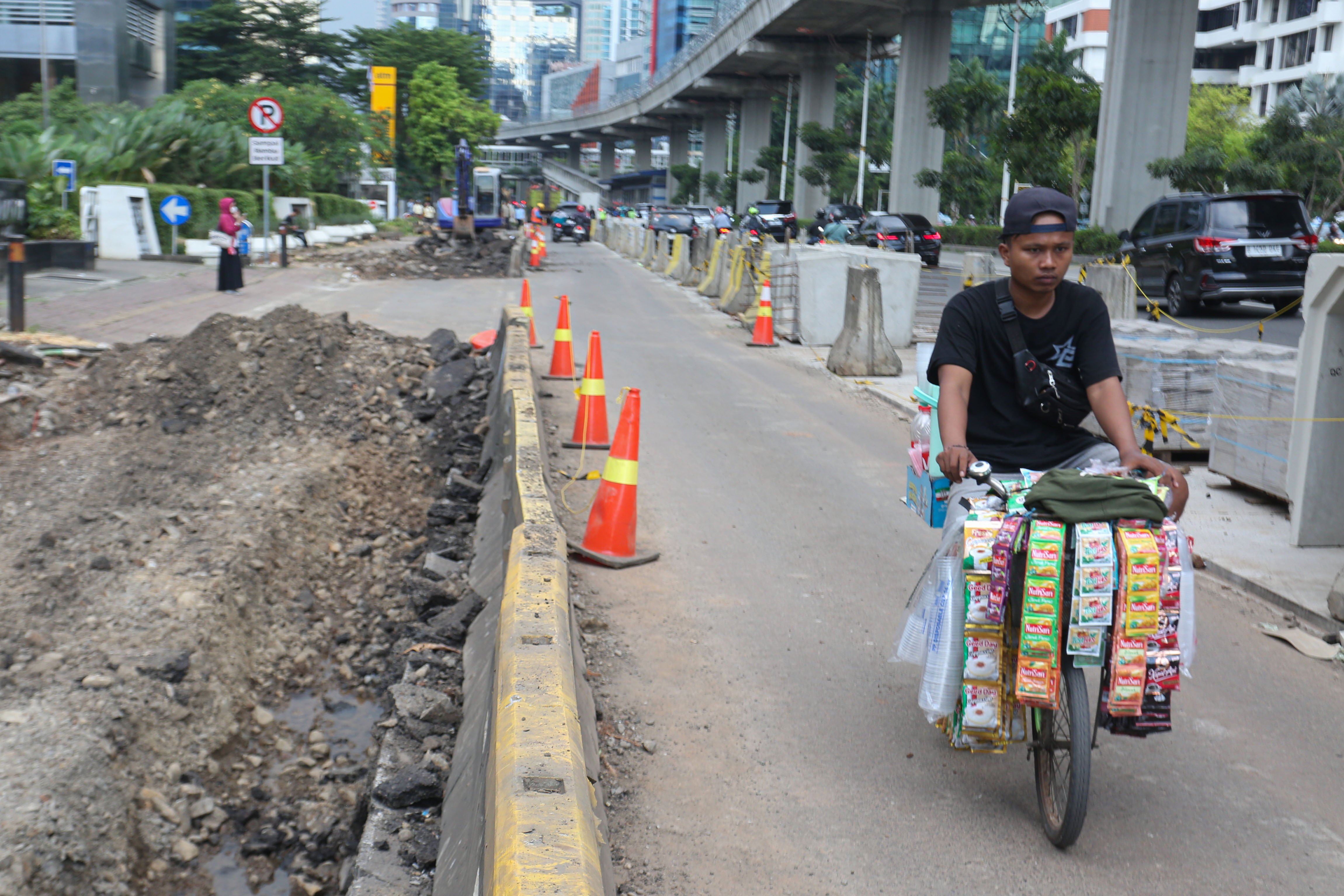 Pedagang yang menggunakan sepeda melintas di dekat proyek revitalisasi Jalan H.R. Rasuna Said, Kuningan, Jakarta Selatan, Selasa (14/4/2026). Penataan jalan sepanjang 3,65 kilometer yang dimulai dari Jalan Gembira hingga Simpang Kuningan itu bertujuan untuk membuat ruang bersama yang inklusif dengan memperhatikan seluruh pengguna jalan mulai dari pejalan kaki, pesepeda, pengguna transportasi umum hingga kendaraan bermotor.