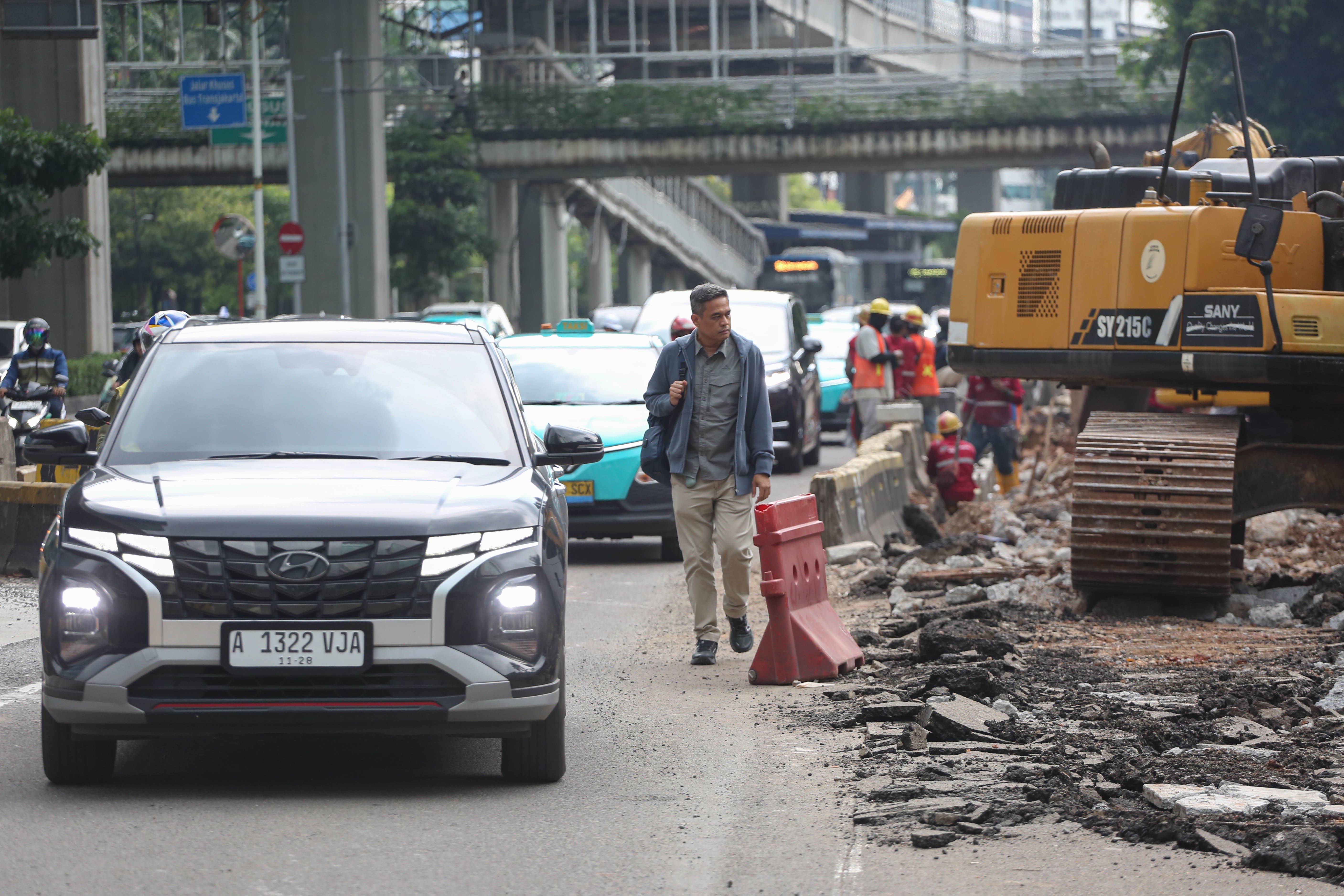 Pejalan kaki dan pengendara mobil melintas di dekat proyek revitalisasi Jalan H.R. Rasuna Said, Kuningan, Jakarta Selatan, Selasa (14/4/2026). Penataan jalan sepanjang 3,65 kilometer yang dimulai dari Jalan Gembira hingga Simpang Kuningan itu bertujuan untuk membuat ruang bersama yang inklusif dengan memperhatikan seluruh pengguna jalan mulai dari pejalan kaki, pesepeda, pengguna transportasi umum hingga kendaraan bermotor.
