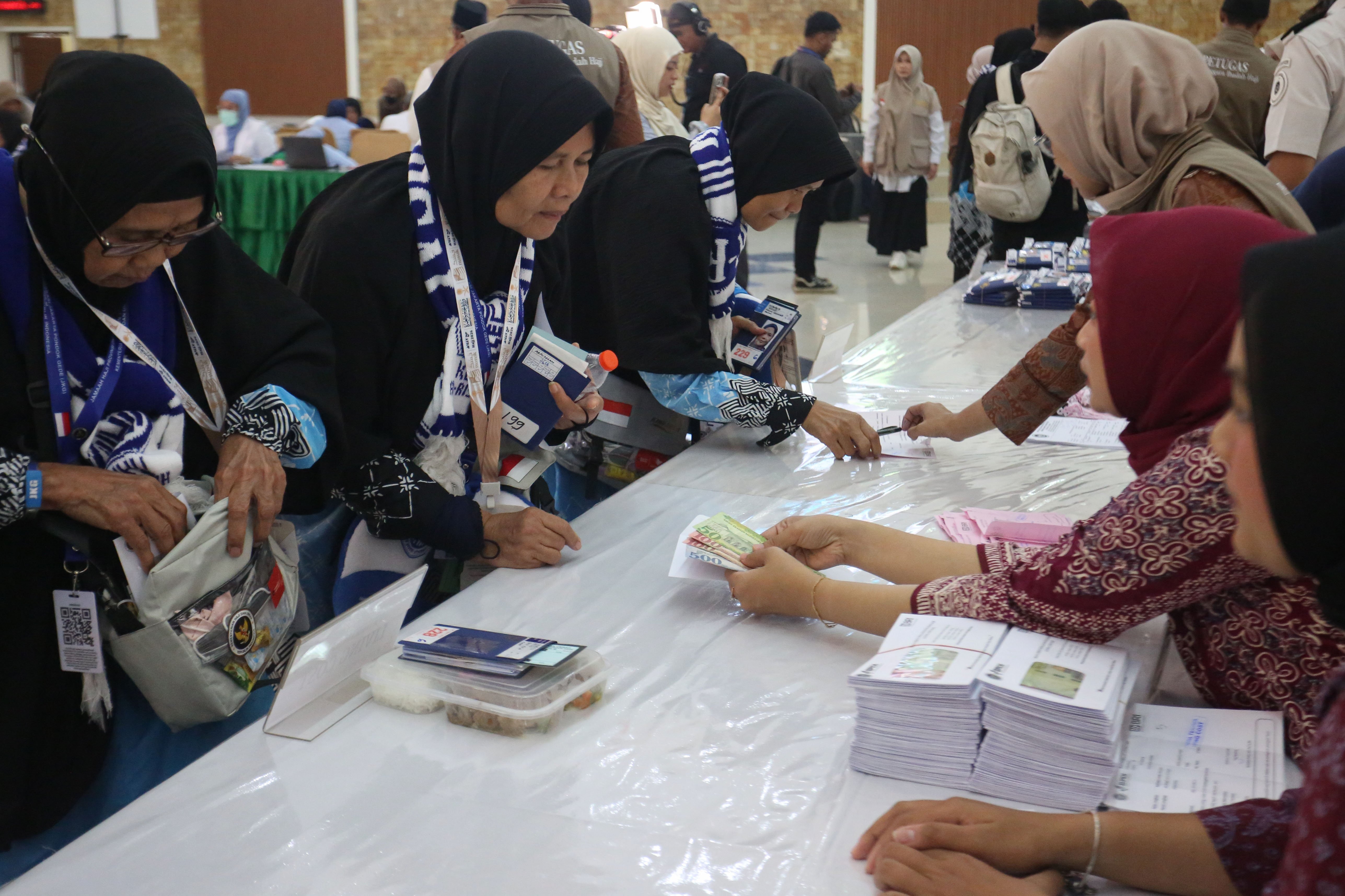 Petugas Penyelenggara Ibadah Haji (PPIH) memberikan uang saku kepada jamaah calon haji di Asrama Haji Pondok Gede, Jakarta, Selasa (21/4/2026). Sebanyak 393 jamaah calon haji kloter pertama asal Jakarta mengikuti pemeriksaan administrasi dan kesehatan sebelum diberangkatkan ke tanah suci pada 22 April 2026.