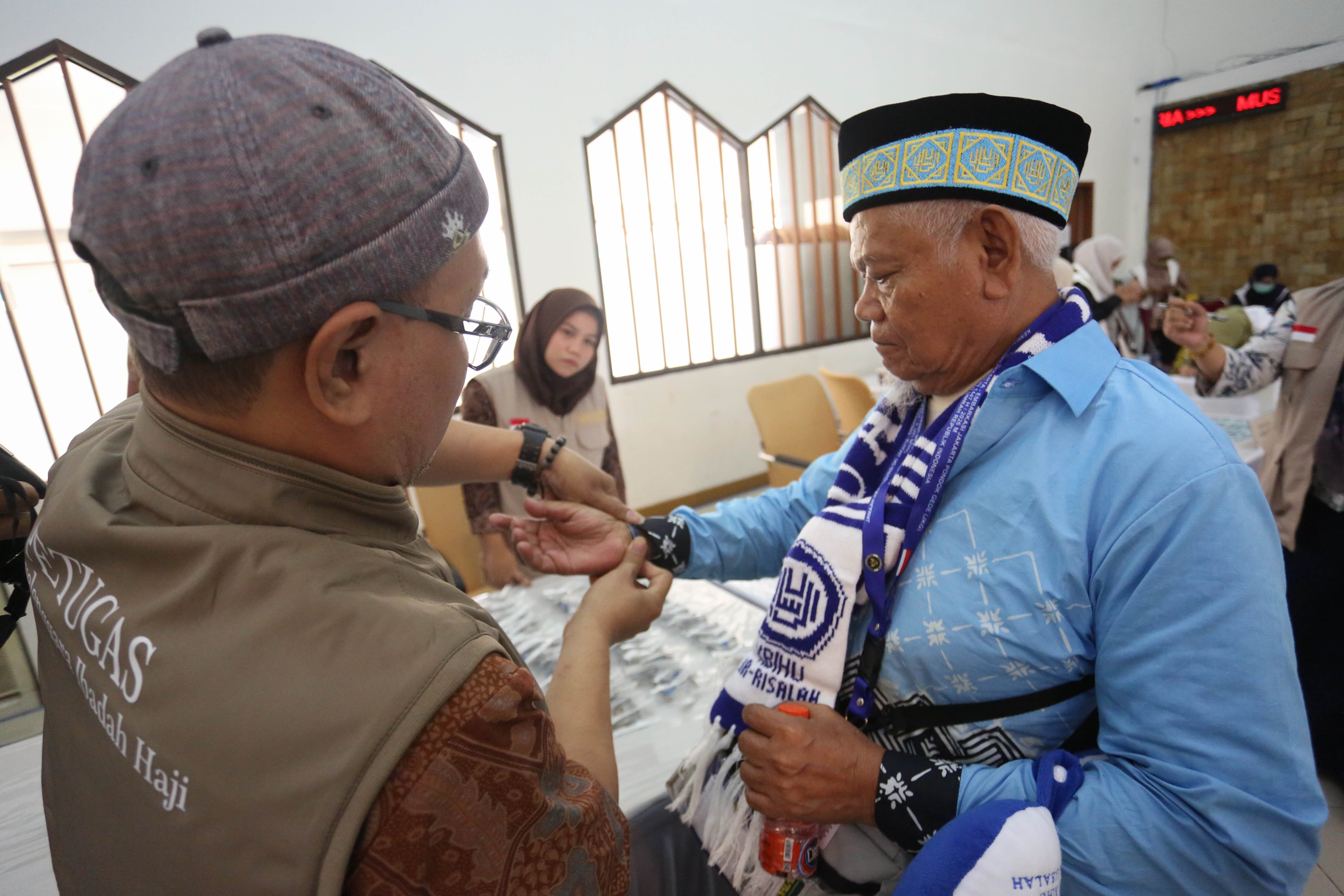 Petugas Penyelenggara Ibadah Haji (PPIH) memasangkan gelang identitas kepada jamaah calon haji di Asrama Haji Pondok Gede, Jakarta, Selasa (21/4/2026). Sebanyak 393 jamaah calon haji kloter pertama asal Jakarta mengikuti pemeriksaan administrasi dan kesehatan sebelum diberangkatkan ke tanah suci pada 22 April 2026.
