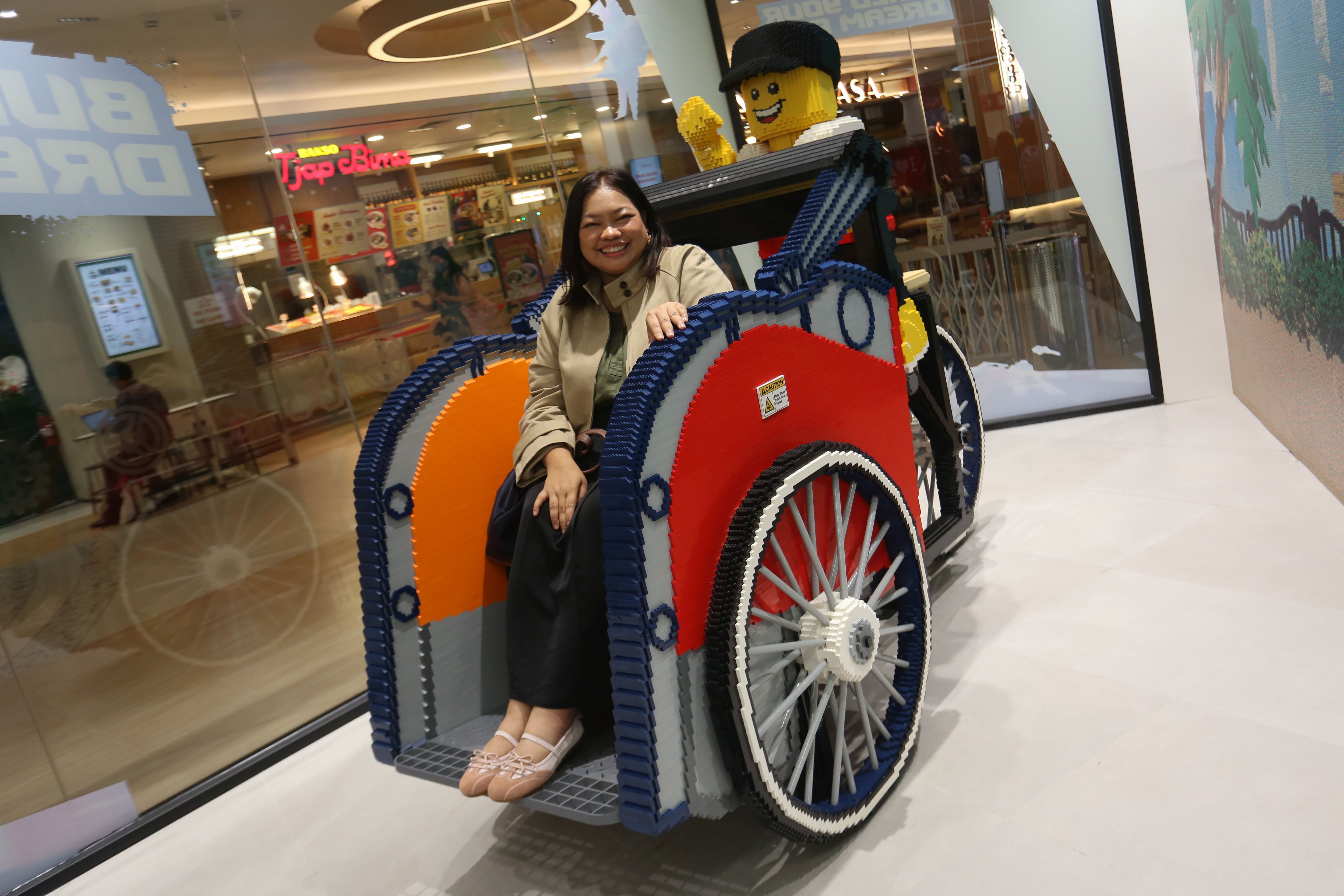 Pengunjung menaiki instalasi LEGO berbentuk becak yang ditampilkan di LEGO Certified Store, Grand Indonesia East Mall, Jakarta, Jumat (24/4/2026). Gerai LEGO terbesar di Asia Tenggara ini dirancang menjadi spot bermain yang kreatif bagi anak-anak, keluarga dan para penggemar dengan menghadirkan pengalaman eksklusif melalui Minifigure Factory serta instalasi yang terinspirasi budaya Indonesia yakni komodo dan becak.