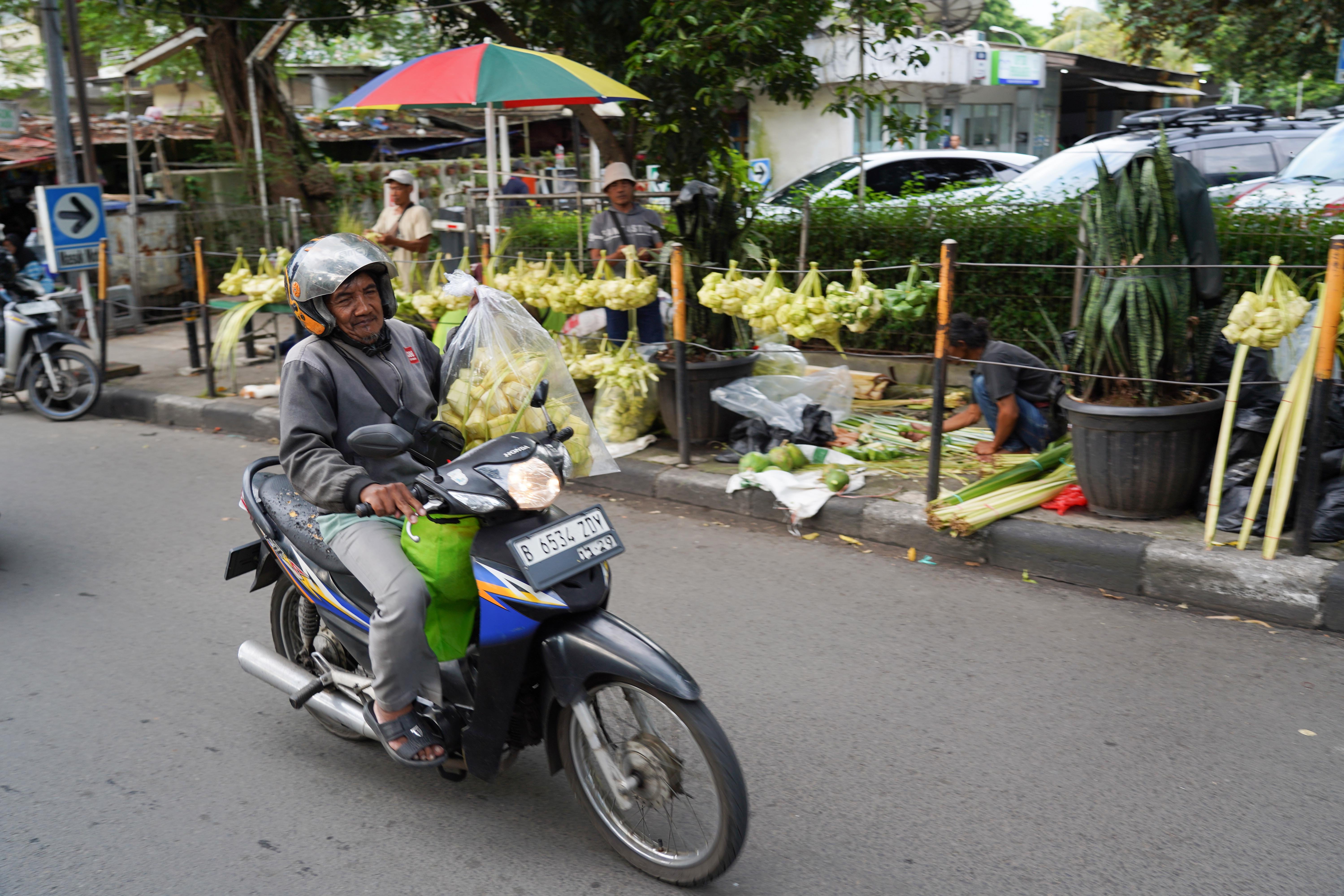 Warga membawa ketupat yang telah dibelinya di Pasar Pondok Labu, Jakarta Selatan, Senin (25/5/2026). Ketupat tersebut dijual Rp 10 ribu per ikatnya atau Rp 1.000 per ketupat dan untuk daunnya saja yang belum dianyam dihargai Rp 500 per helai.