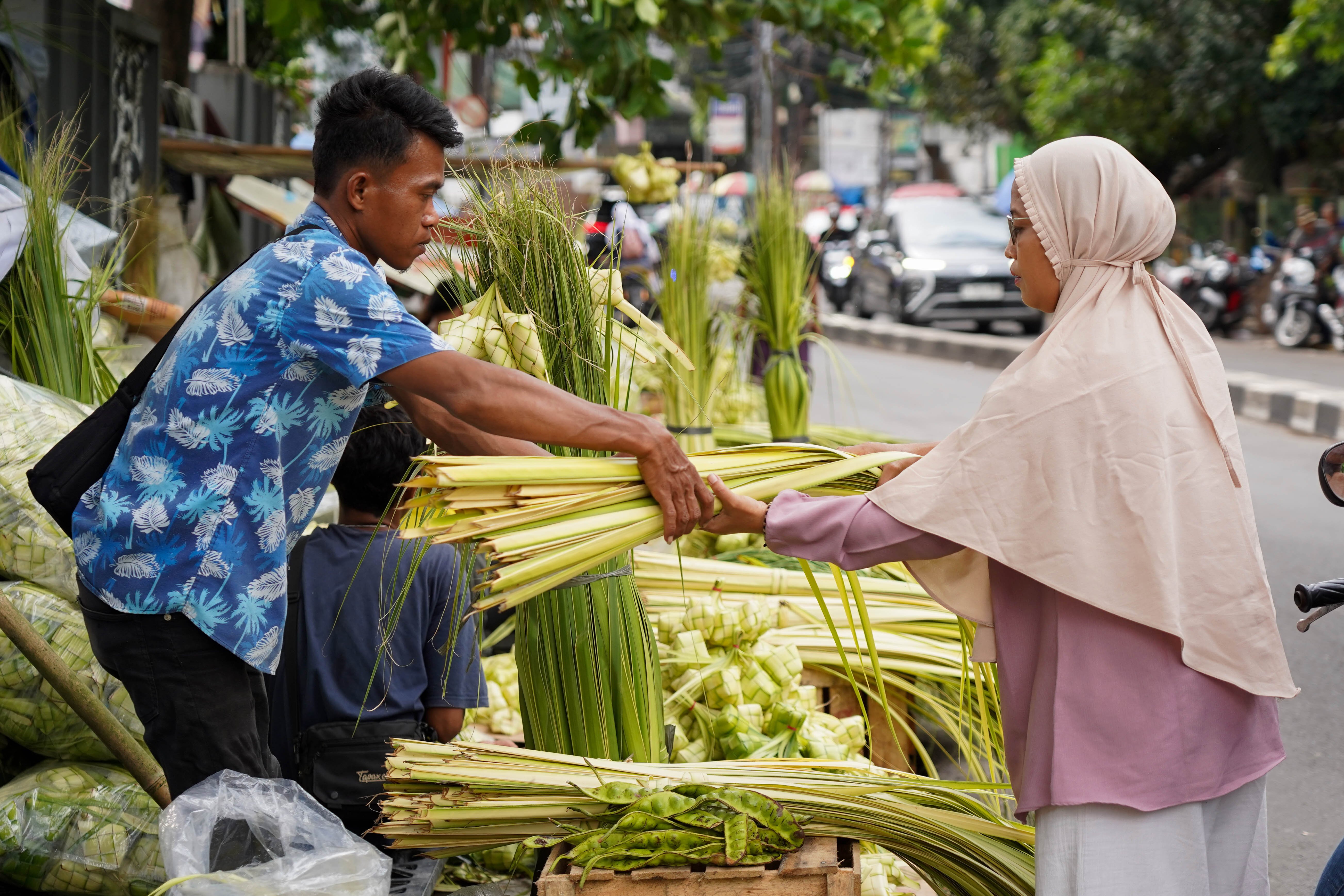 Pedagang melayani calon pembeli yang hendak membeli ketupat di Pasar Pondok Labu, Jakarta Selatan, Senin (25/5/2026). Ketupat tersebut dijual Rp 10 ribu per ikatnya atau Rp 1.000 per ketupat dan untuk daunnya saja yang belum dianyam dihargai Rp 500 per helai.