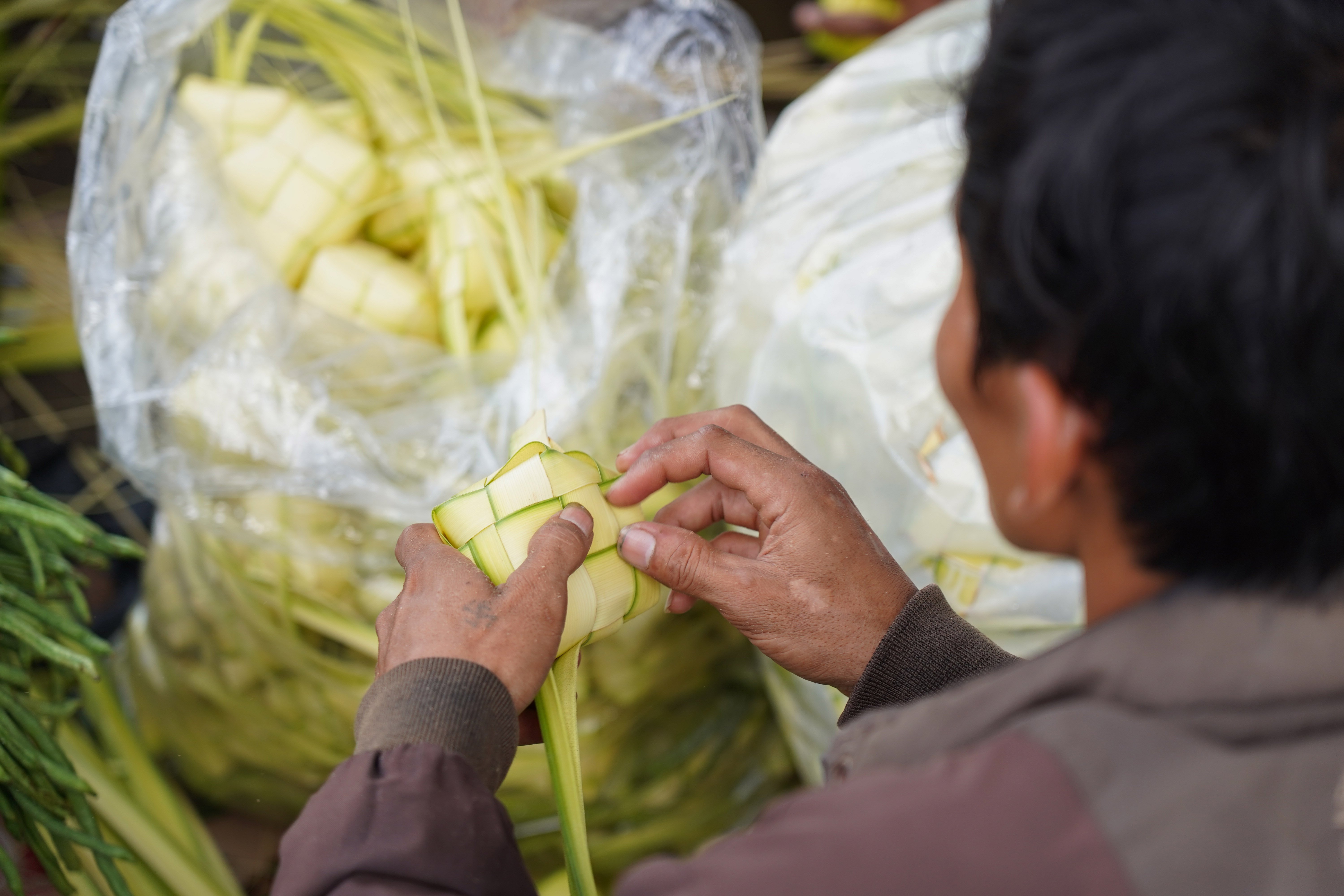 Pedagang menganyam ketupat yang dijualnya di Pasar Pondok Labu, Jakarta Selatan, Senin (25/5/2026). Ketupat tersebut dijual Rp 10 ribu per ikatnya atau Rp 1.000 per ketupat dan untuk daunnya saja yang belum dianyam dihargai Rp 500 per helai.