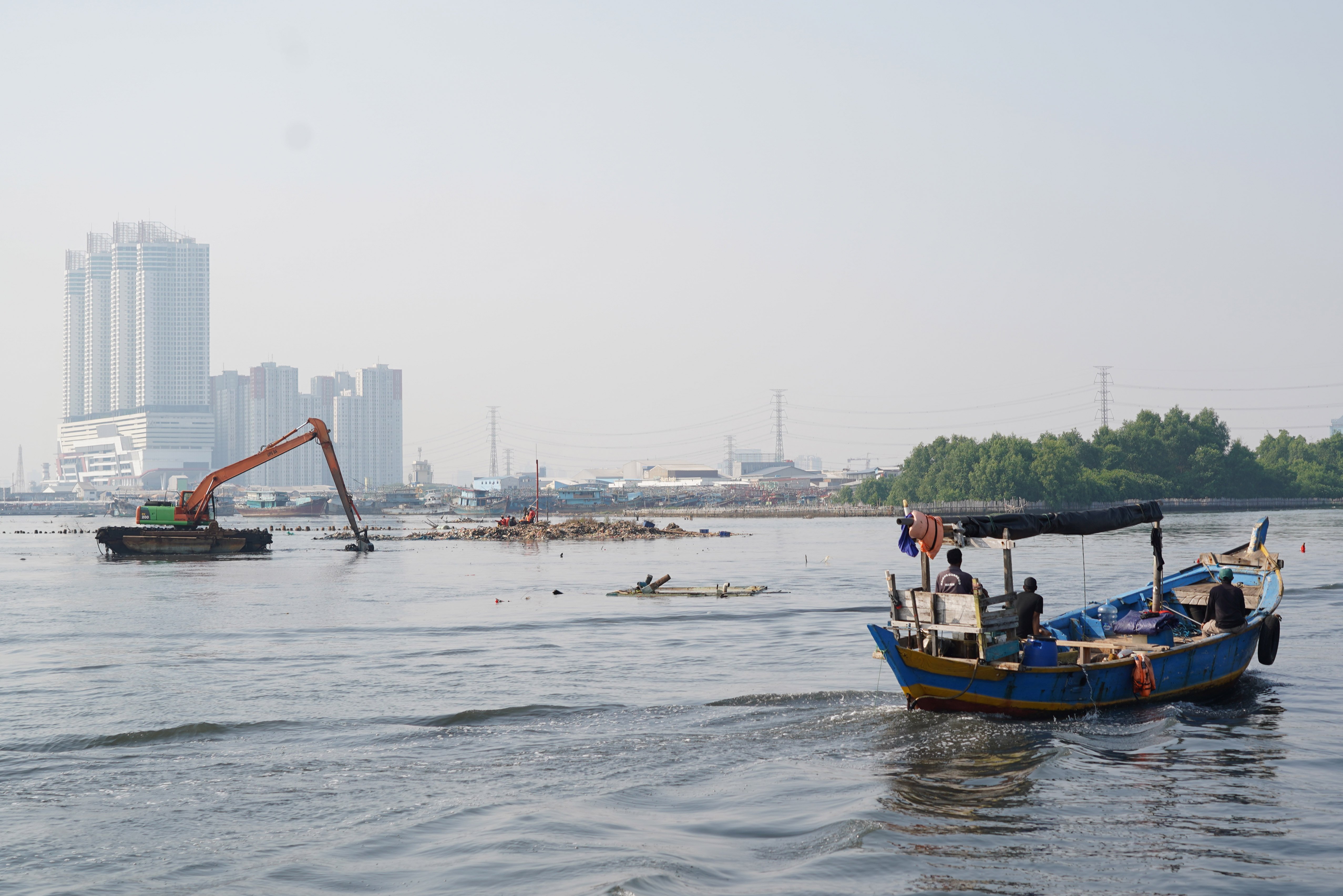 Perahu nelayan melintas di dekat aktivitas pengangkutan sampah yang menumpuk di pesisir laut kawasan Muara Angke, Jakarta Utara, Senin (8/6/2026). Pembersihan tersebut dilakukan guna menagani sampah agar tidak mencemari lingkungan laut dan kawasan di sekitarnya serta menggangu aktivitas nelayan.