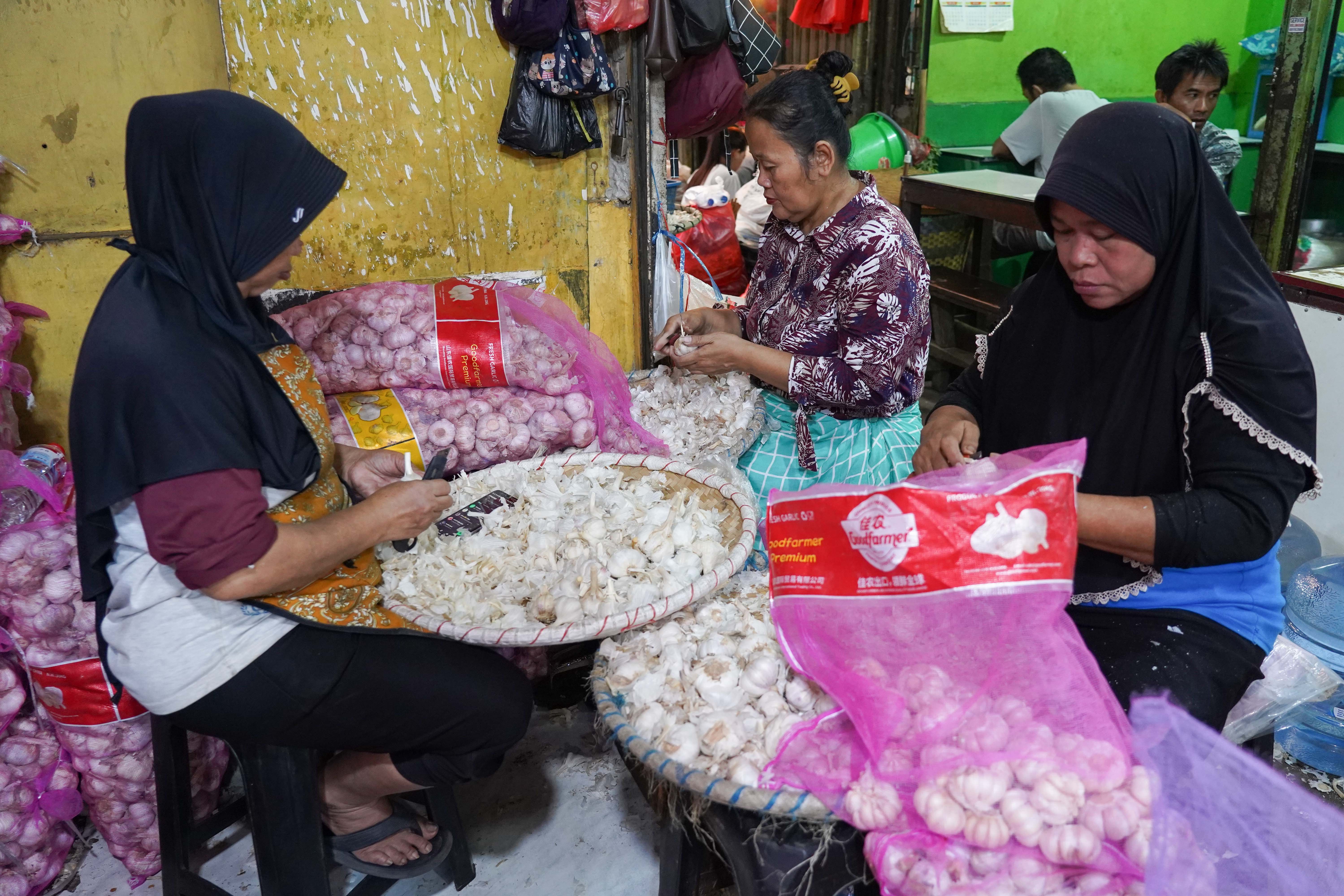 Pekerja mengupas kulit bawang putih impor yang dijual di Pasar Induk Kramat Jati, Jakarta, Selasa (14/7/2026). Berdasarkan pemantauan Indeks Perkembangan Harga (IPH), rata-rata harga bawang putih secara nasional kini mencapai Rp 42.611 per kilogram atau sudah berada jauh di atas Harga Acuan Penjualan (HAP) konsumen. Kenaikan ini disebabkan oleh melemahnya nilai tukar rupiah terhadap dolar Amerika Serikat (AS) dan meningkatnya biaya logistik internasional.