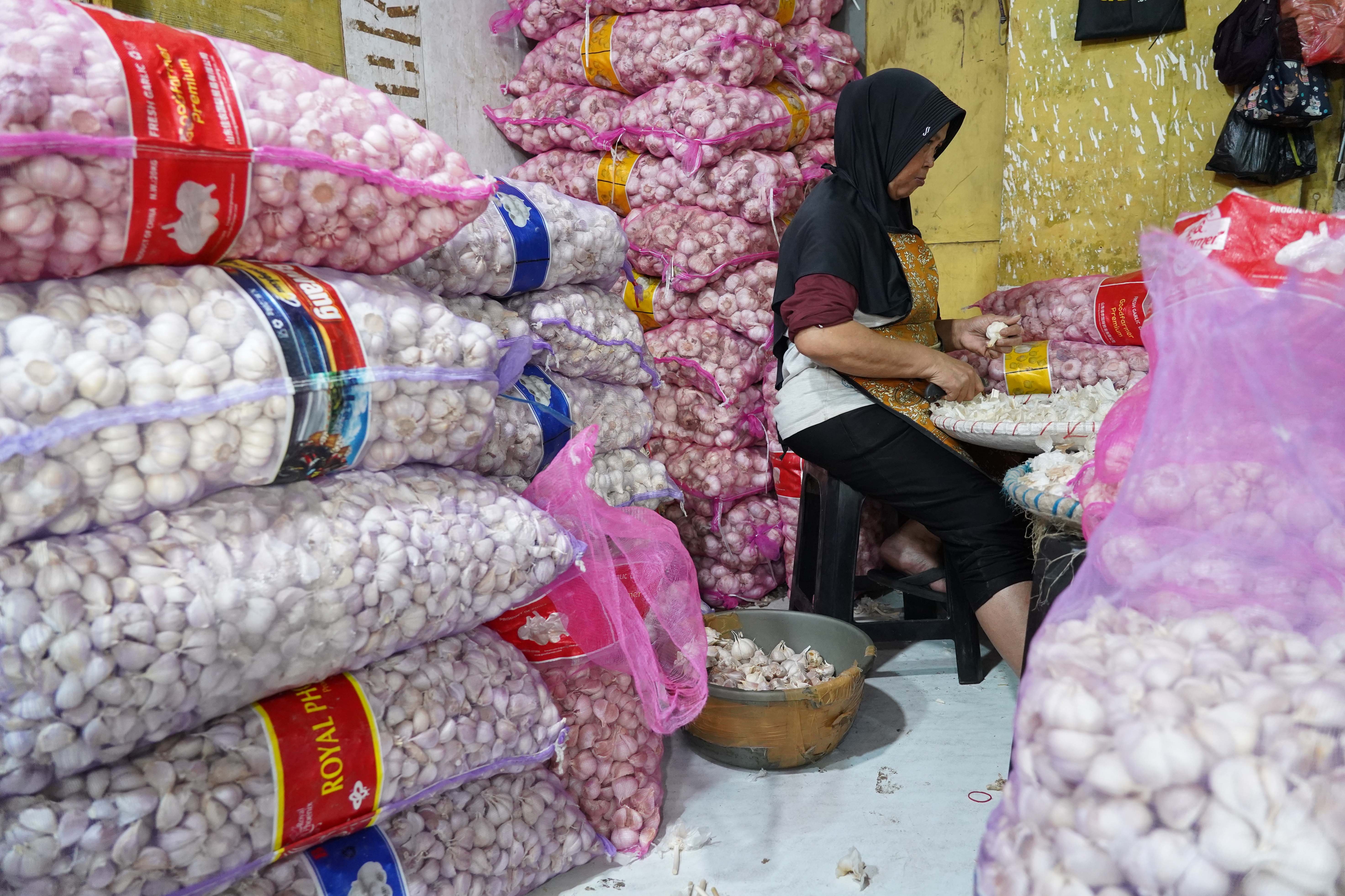 Pekerja mengupas kulit bawang putih impor yang dijual di Pasar Induk Kramat Jati, Jakarta, Selasa (14/7/2026). Berdasarkan pemantauan Indeks Perkembangan Harga (IPH), rata-rata harga bawang putih secara nasional kini mencapai Rp 42.611 per kilogram atau sudah berada jauh di atas Harga Acuan Penjualan (HAP) konsumen. Kenaikan ini disebabkan oleh melemahnya nilai tukar rupiah terhadap dolar Amerika Serikat (AS) dan meningkatnya biaya logistik internasional.