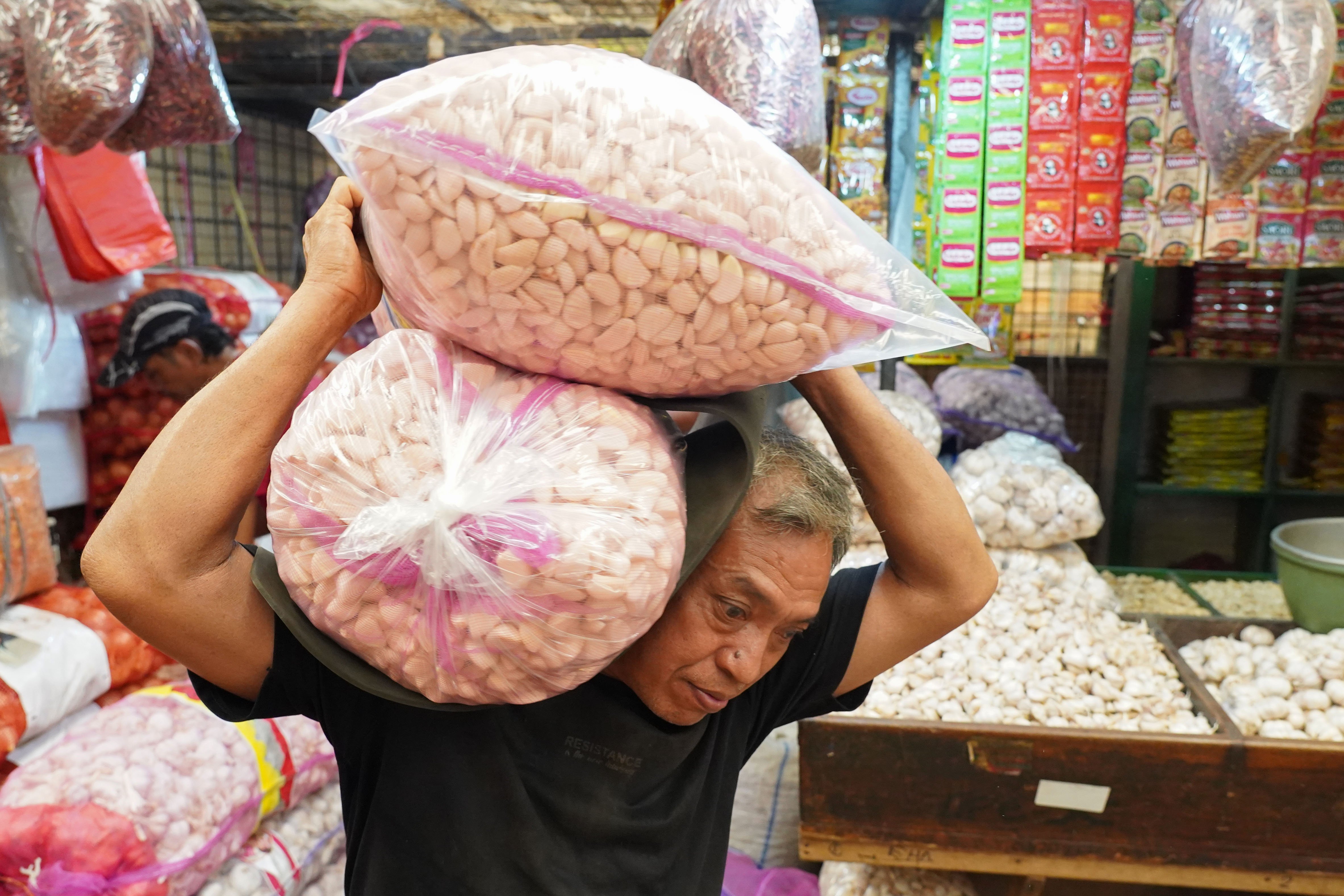 Pekerja memanggul bawang putih impor yang dijual di Pasar Induk Kramat Jati, Jakarta, Selasa (14/7/2026). Berdasarkan pemantauan Indeks Perkembangan Harga (IPH), rata-rata harga bawang putih secara nasional kini mencapai Rp 42.611 per kilogram atau sudah berada jauh di atas Harga Acuan Penjualan (HAP) konsumen. Kenaikan ini disebabkan oleh melemahnya nilai tukar rupiah terhadap dolar Amerika Serikat (AS) dan meningkatnya biaya logistik internasional.